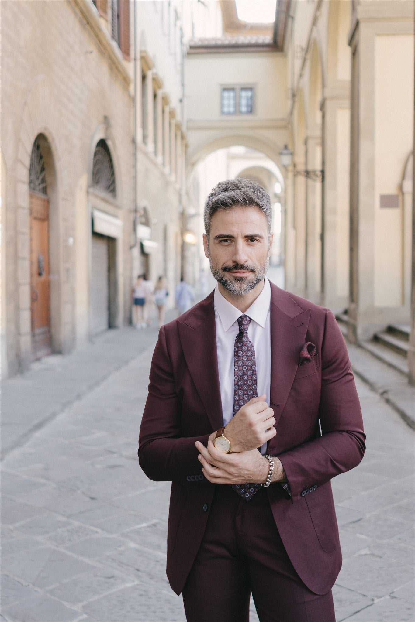 Man in a burgundy suit standing in an alleyway with stone arches.