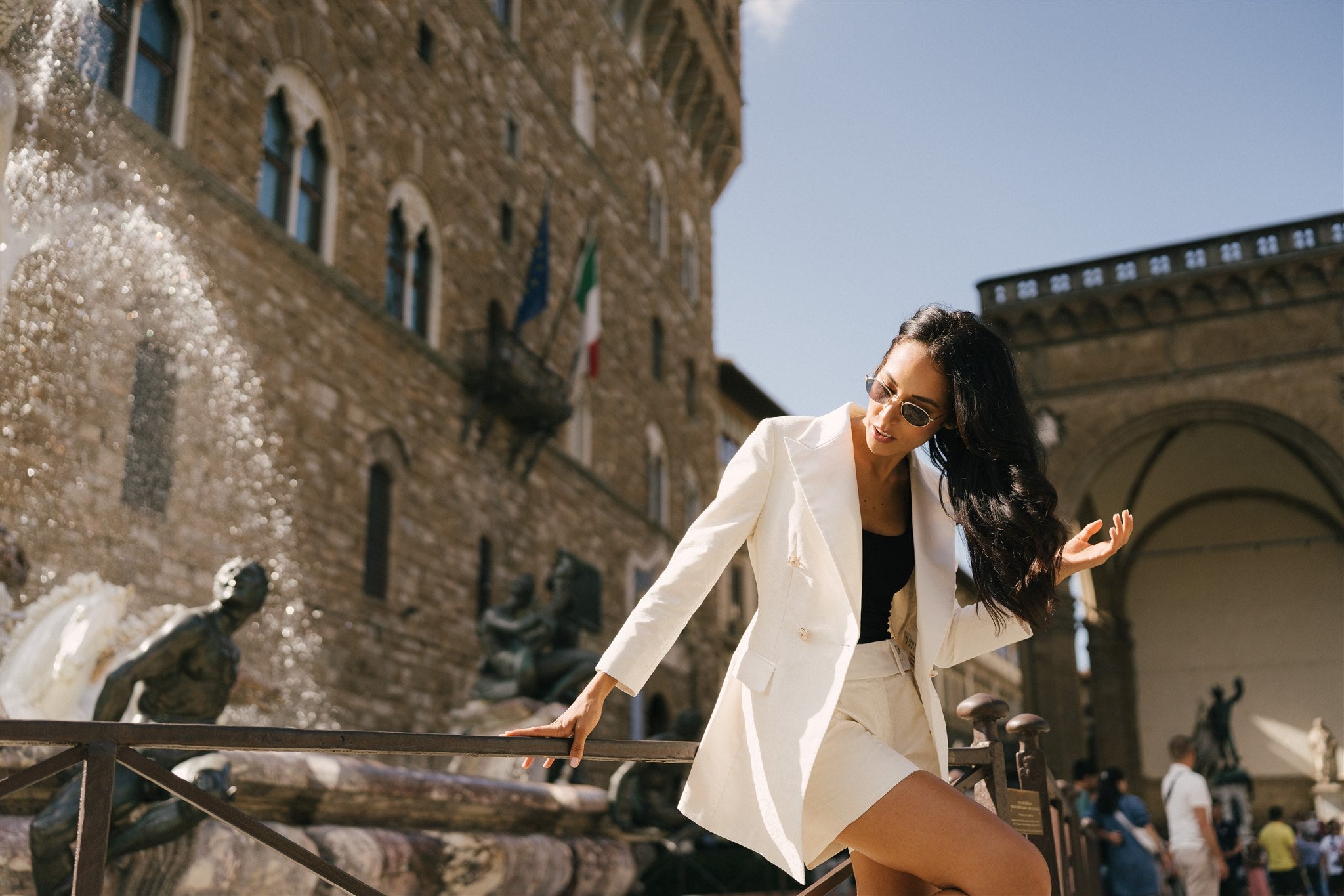 Woman in a white blazer posing in front of a historic building with statues.