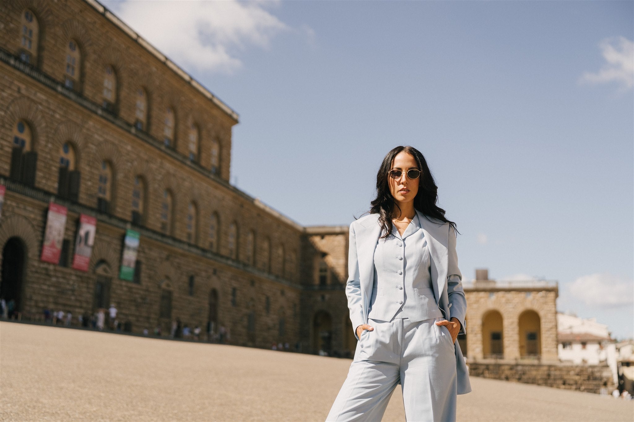 Woman in a light gray suit standing in front of a large stone building with a clear sky.