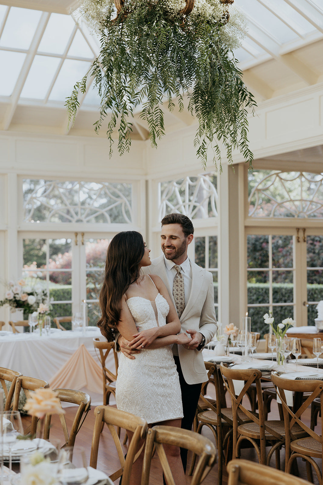 Couple embracing in a wedding reception setting with floral decorations.