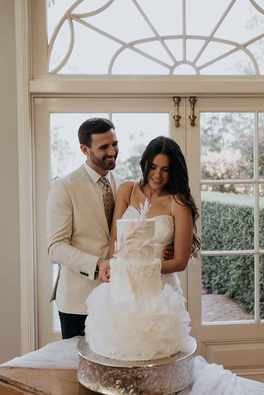 Couple cutting a wedding cake indoors with decorative elements.
