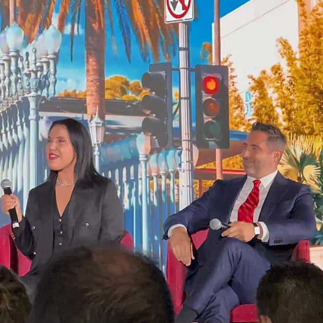 Two people sitting on red chairs with a colorful mural in the background