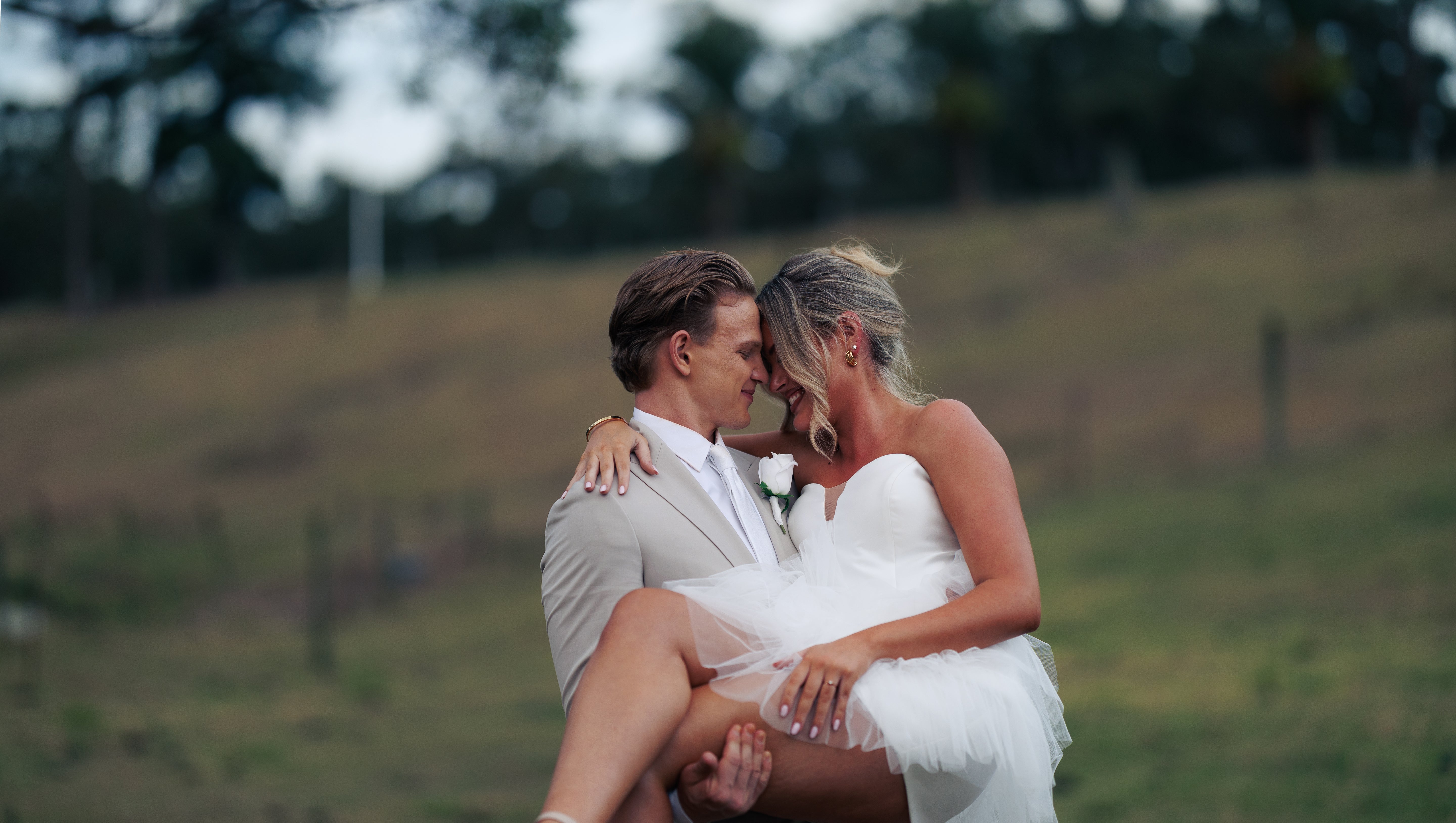Couple in wedding attire embracing in a field with a blurred background