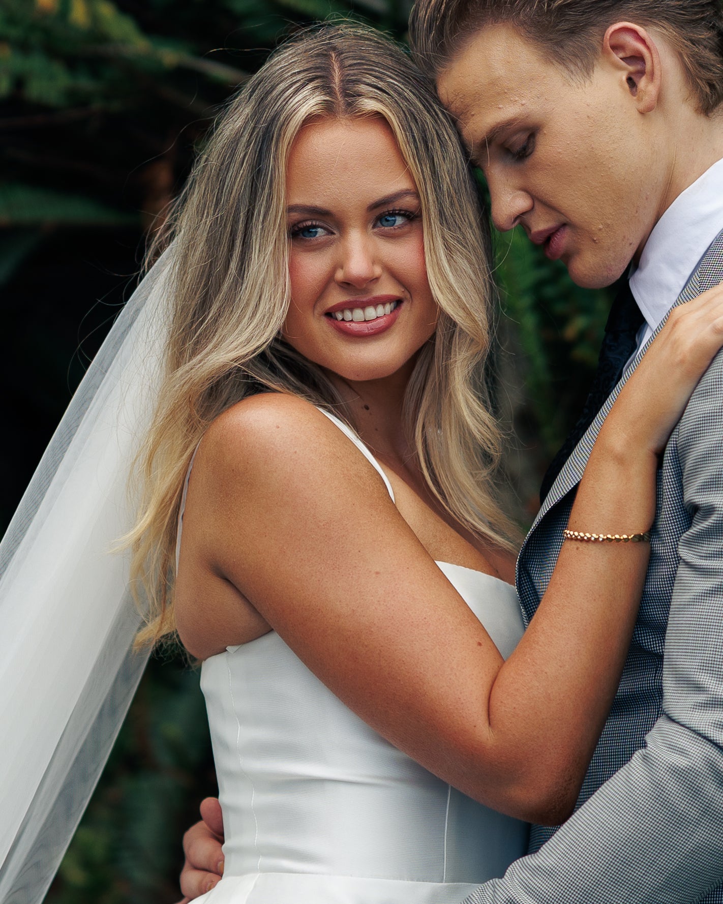 Woman in a white wedding dress embracing a man in a suit with a blurred green background