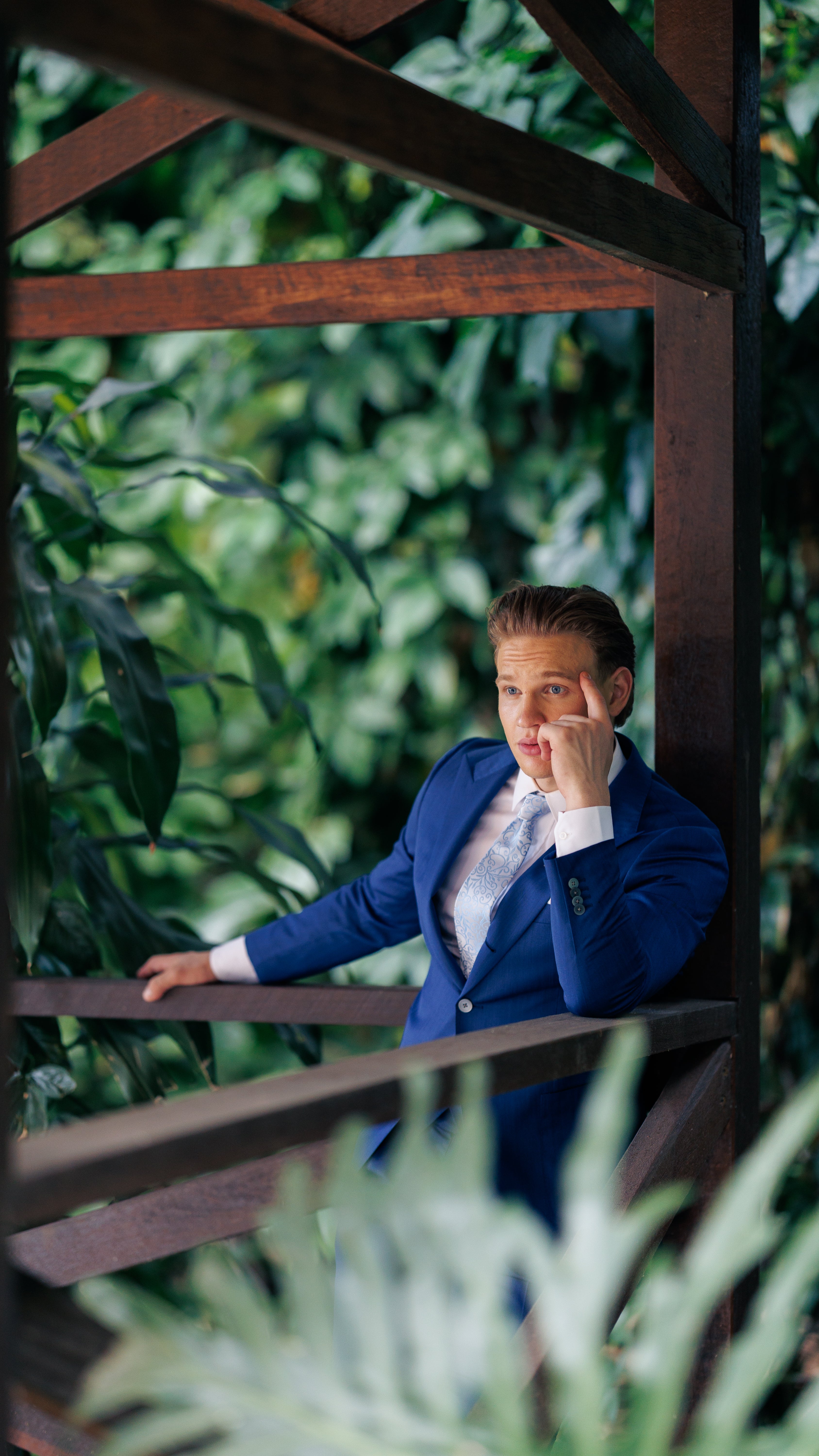 Person in a blue suit sitting on a wooden structure with greenery in the background