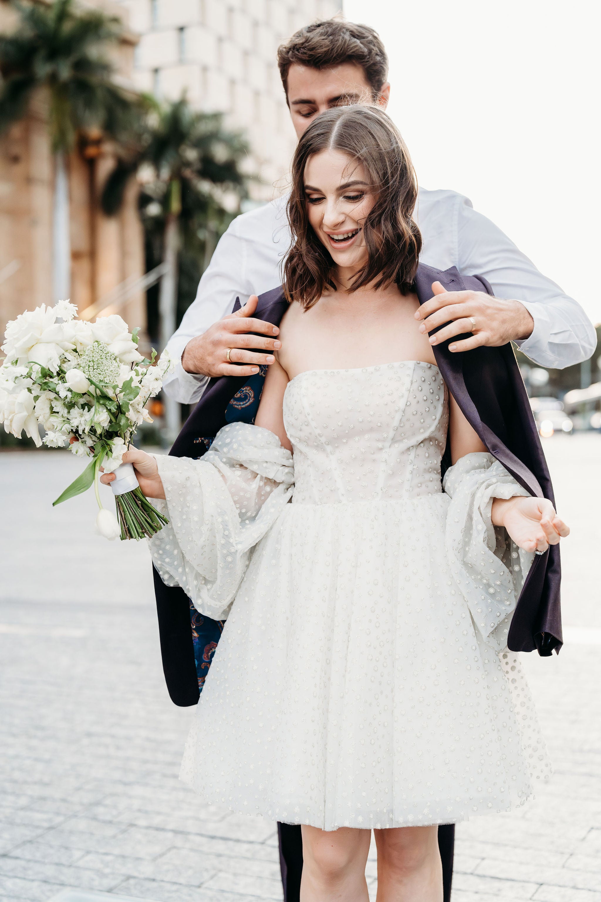 Woman in a wedding dress being helped by a man with a bouquet of flowers.