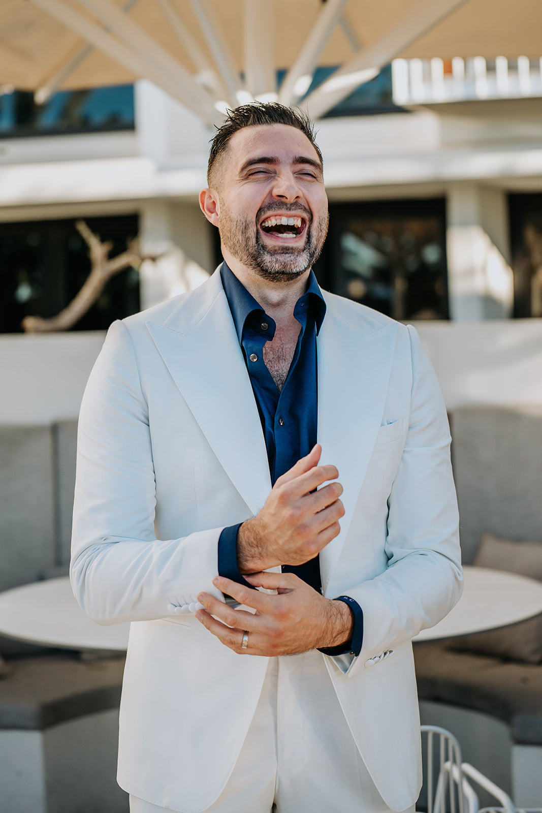 Man in a light gray suit laughing outdoors