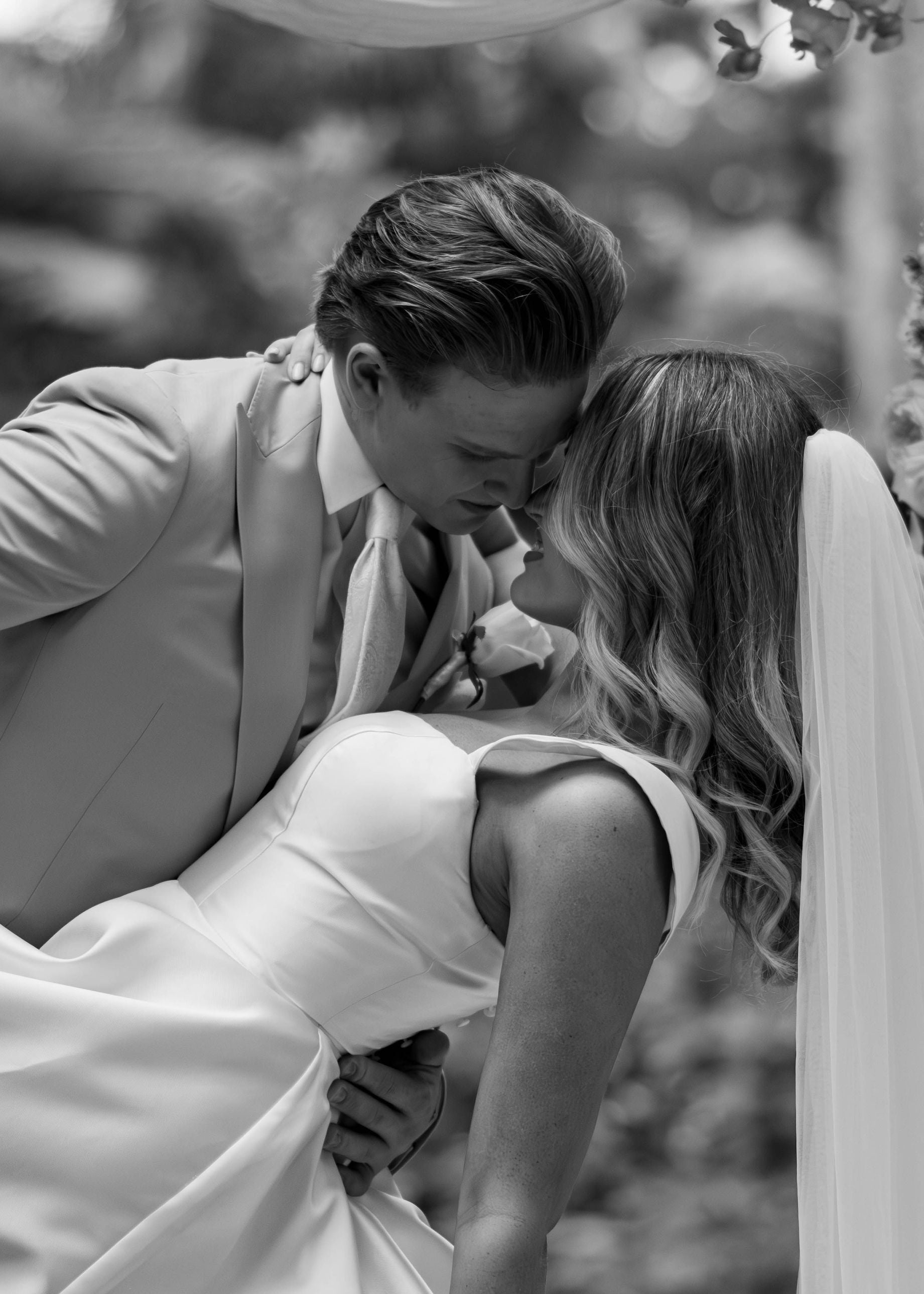 Black and white photo of a couple in wedding attire with a blurred natural background