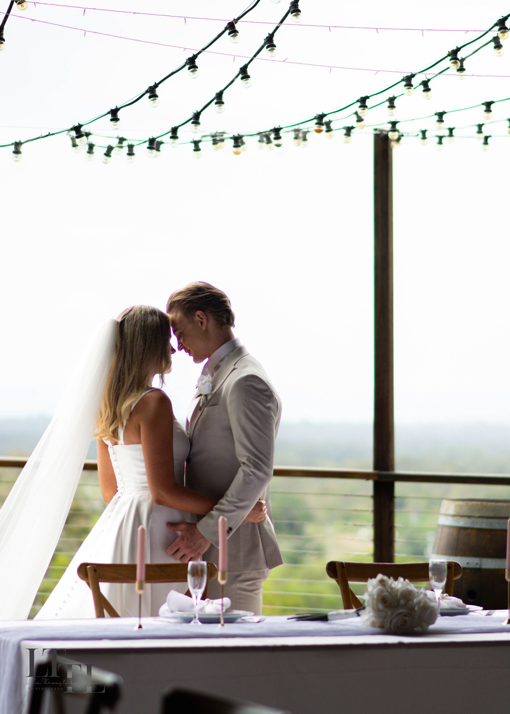 Couple embracing at a wedding table with string lights above
