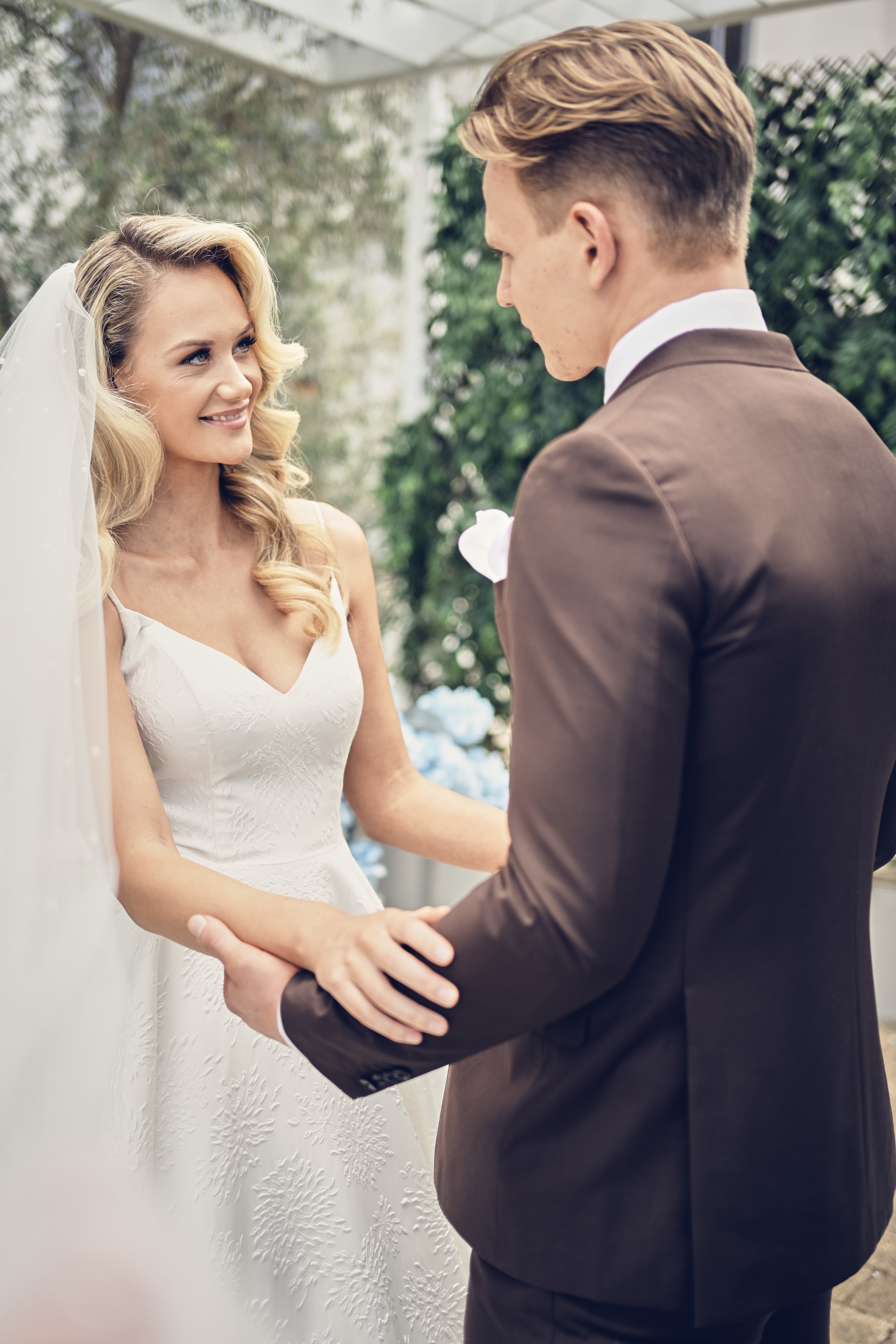Man and woman in wedding attire standing close together outdoors.