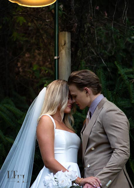 Couple in wedding attire embracing outdoors with greenery in the background