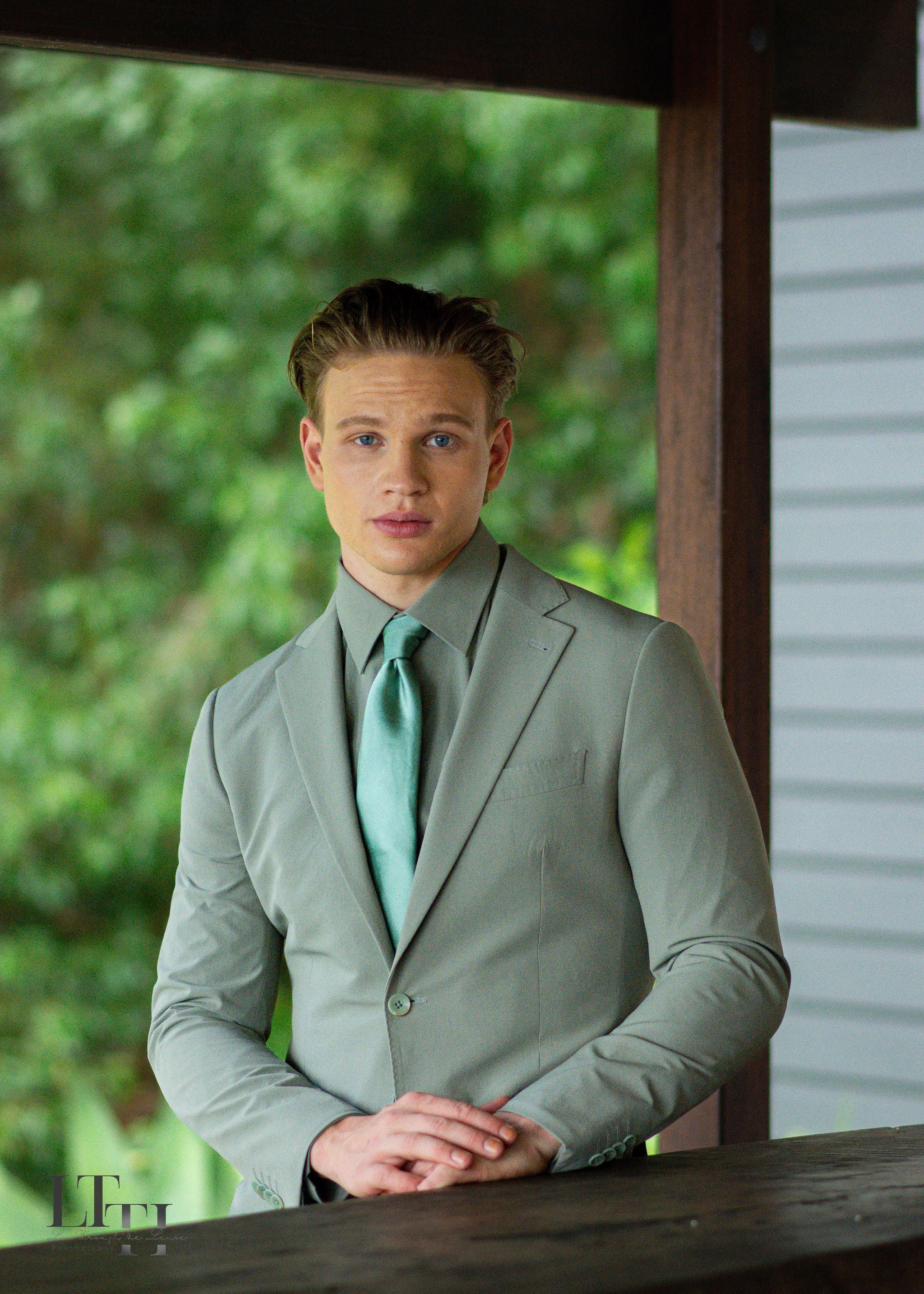 Man in a gray suit with a green tie standing outdoors.