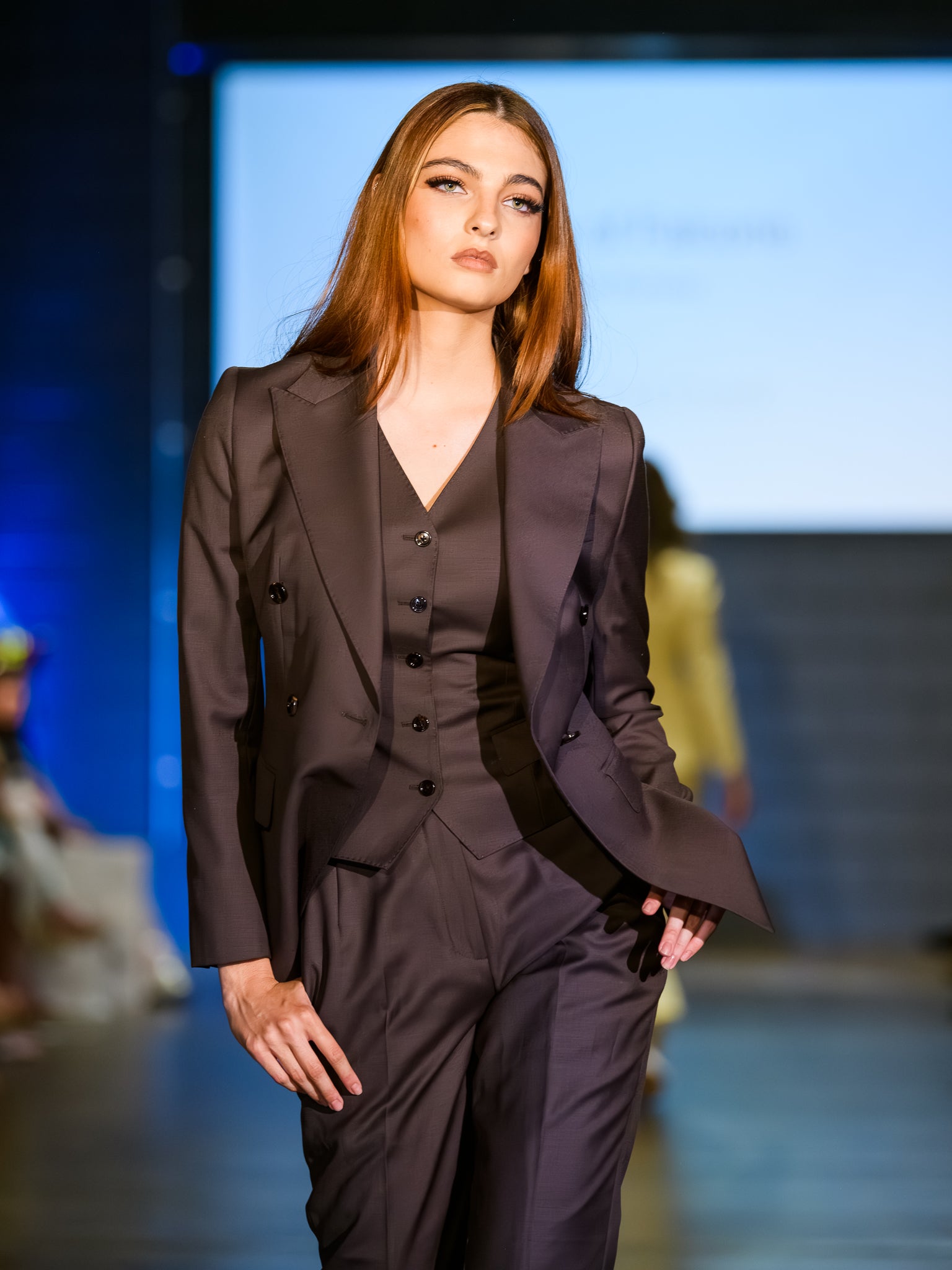 Model wearing a dark suit walking on a runway with a blurred background