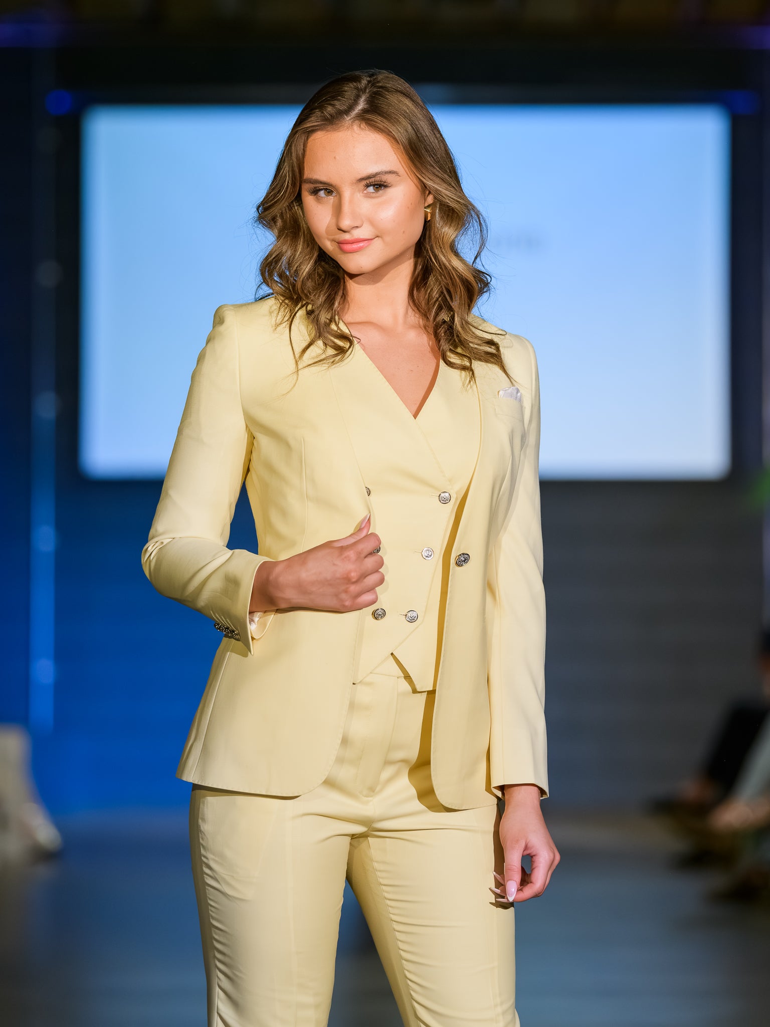 Model wearing a light yellow suit on a runway with a blurred background