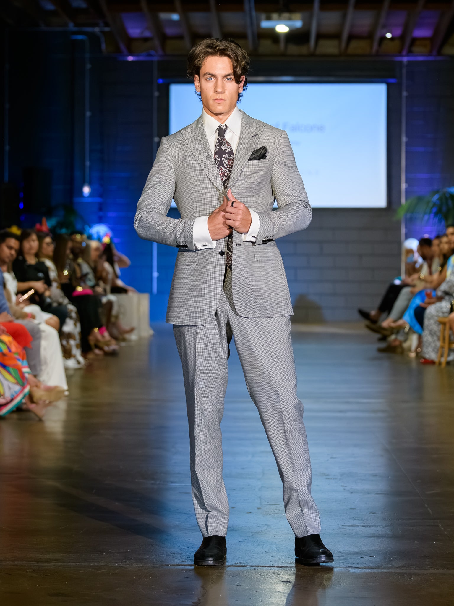 Man in a gray suit walking on a runway at a fashion show.