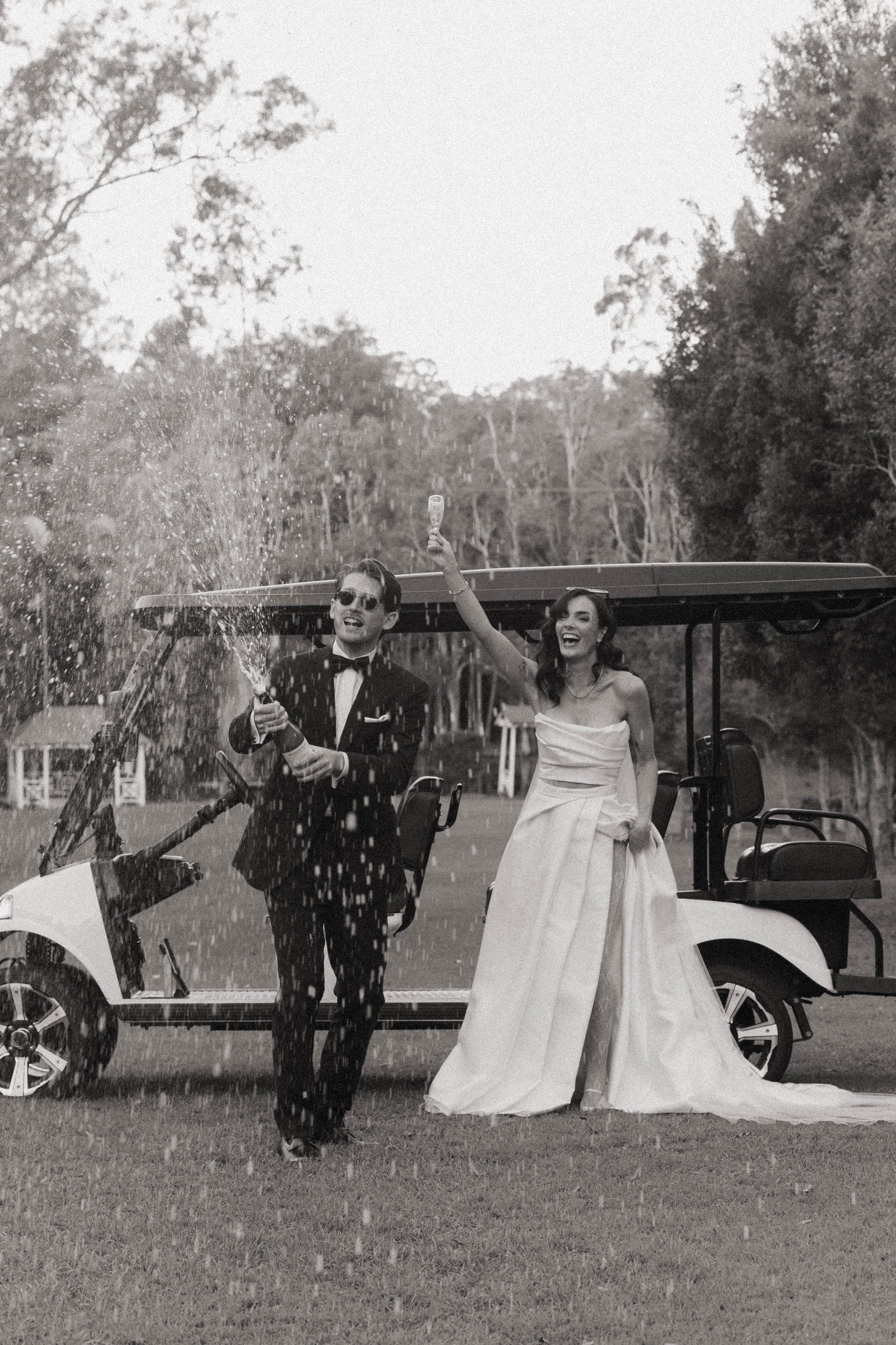 Black and white photo of a couple celebrating with champagne in front of a golf cart.