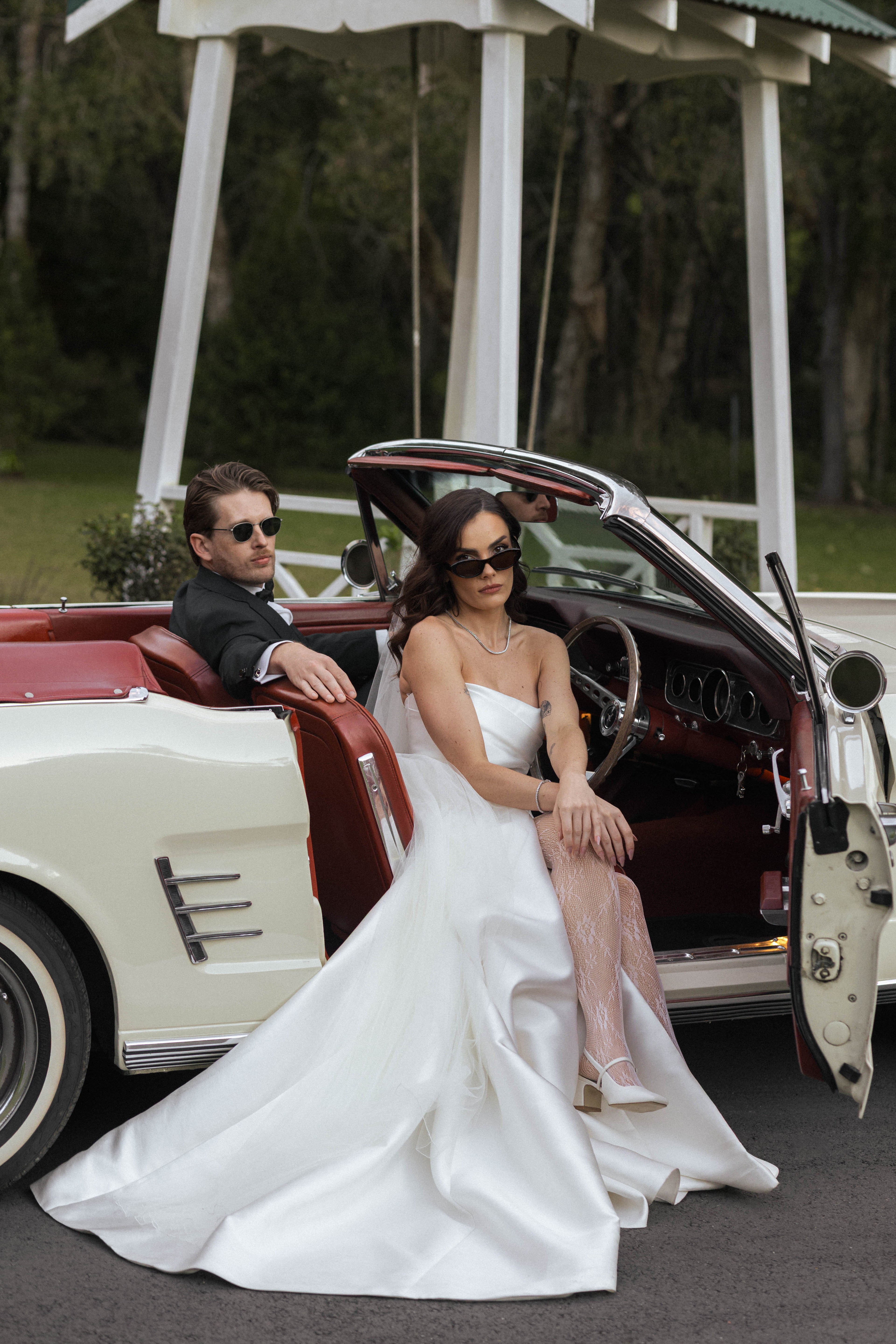 Man and woman in a vintage car, with the woman in a white dress.