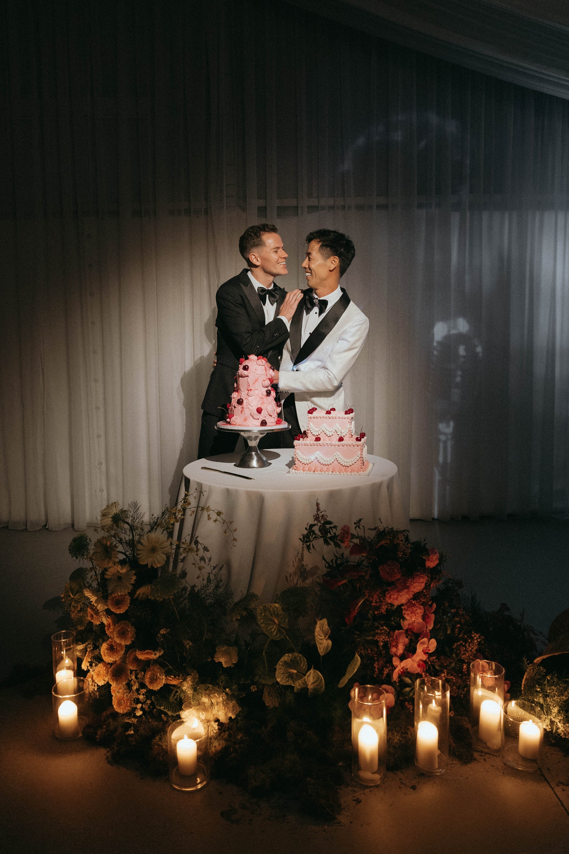 Two people standing behind a table with wedding cakes, surrounded by candles and flowers.
