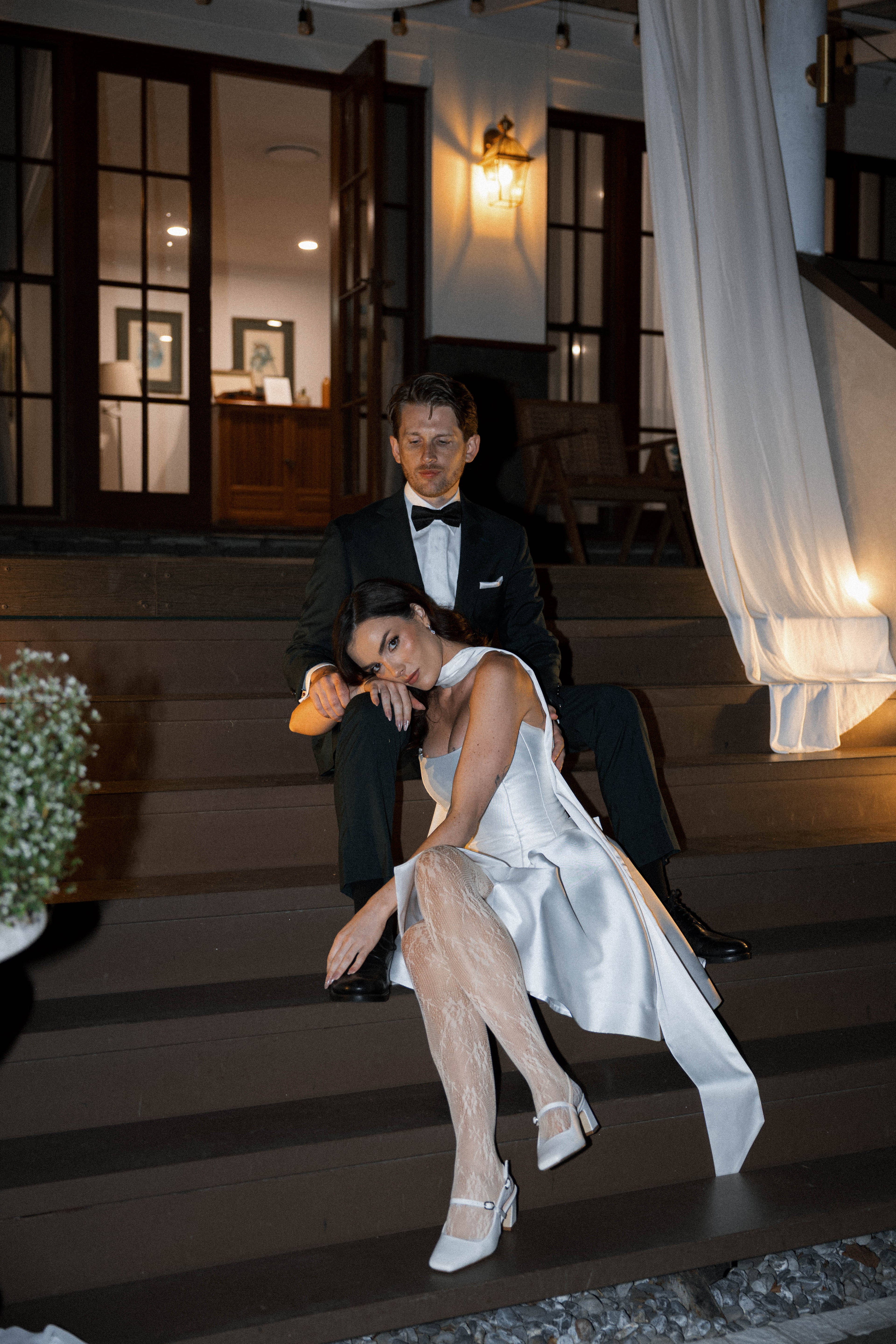 Man and woman in formal attire sitting on a staircase indoors.