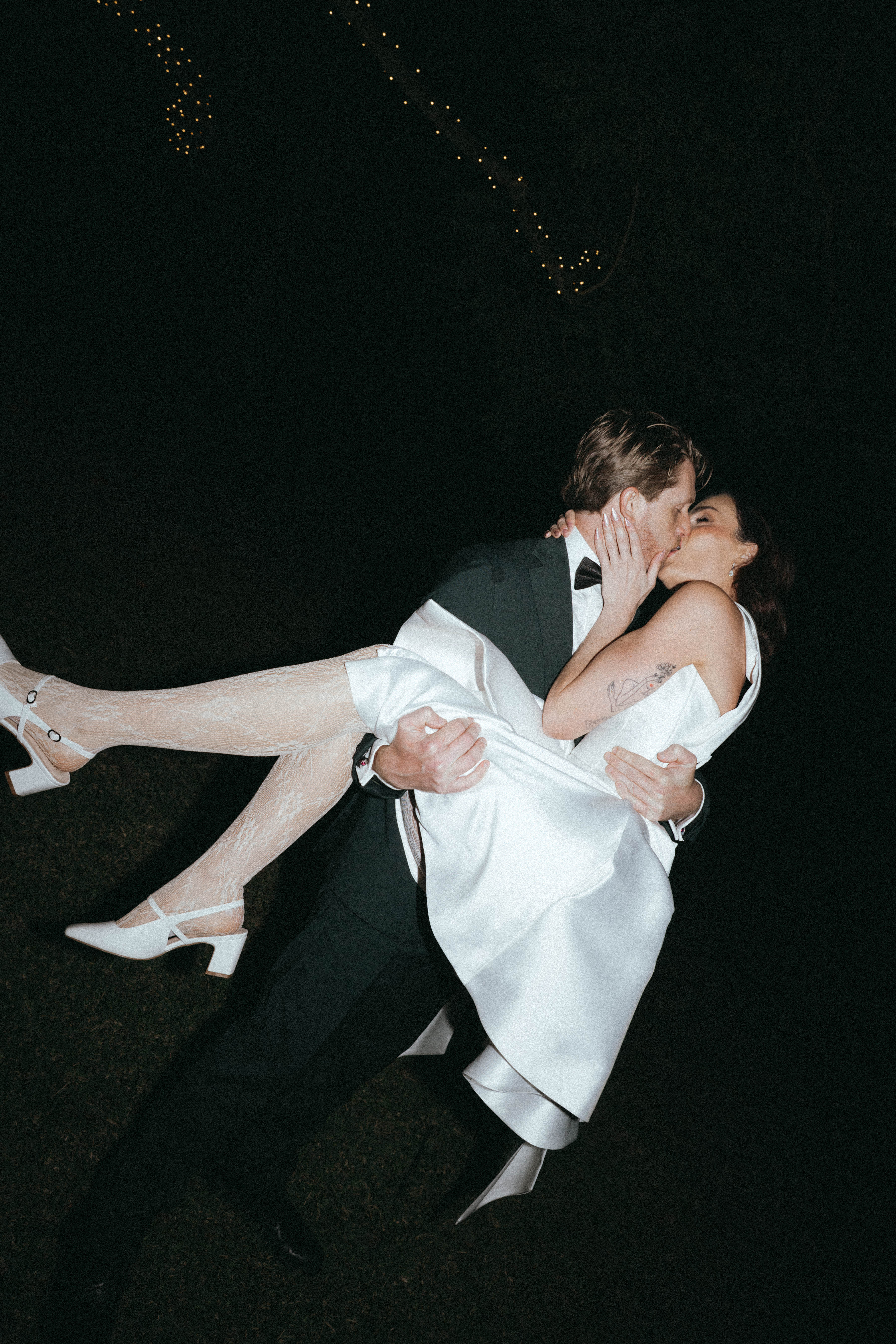 Man in a suit carrying a woman in a white dress against a dark background