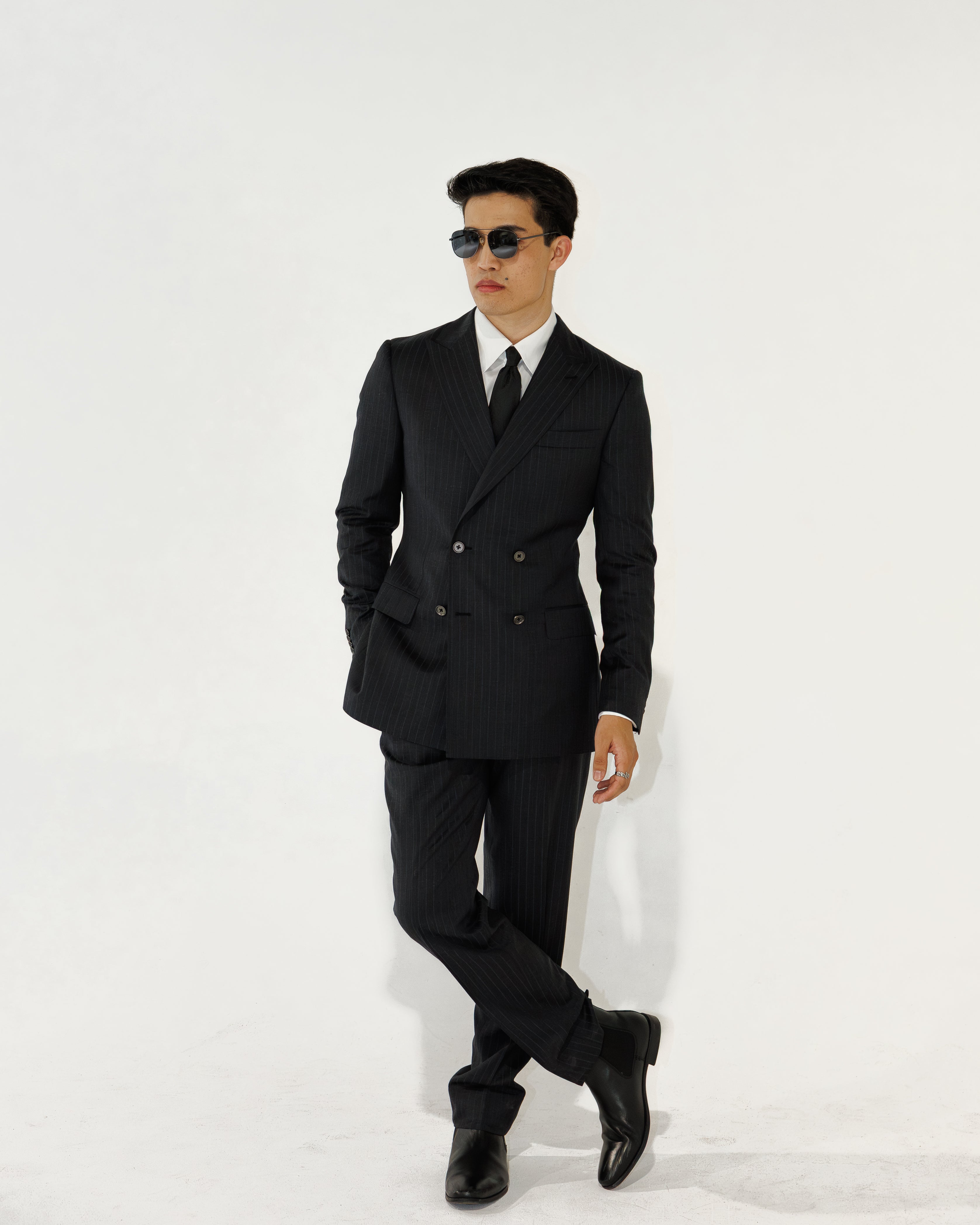 Man wearing a charcoal grey pinstripe  suit and sunglasses on a white background