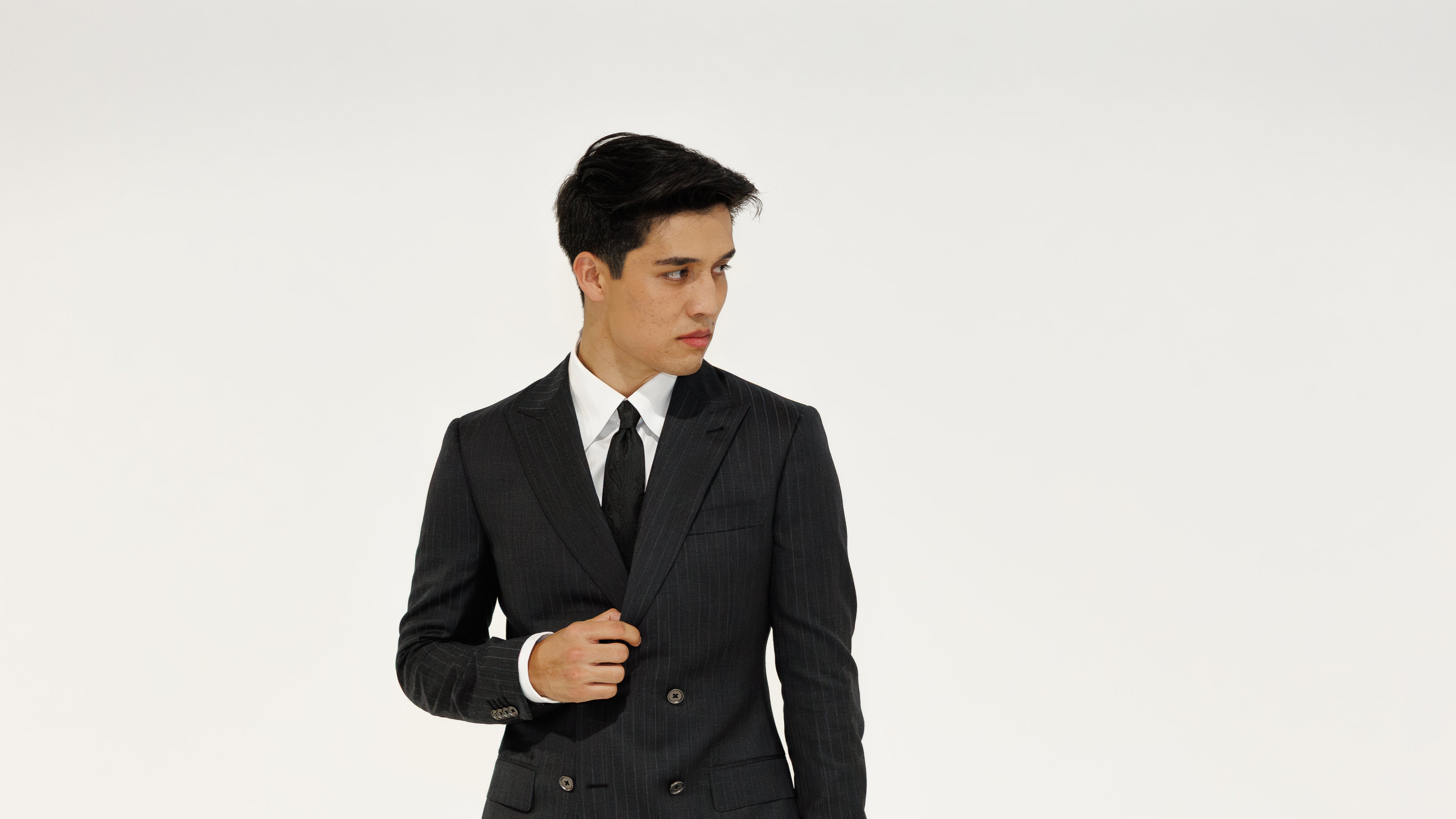 Man wearing a charcoal grey pinstripe  suit and tie on a white background
