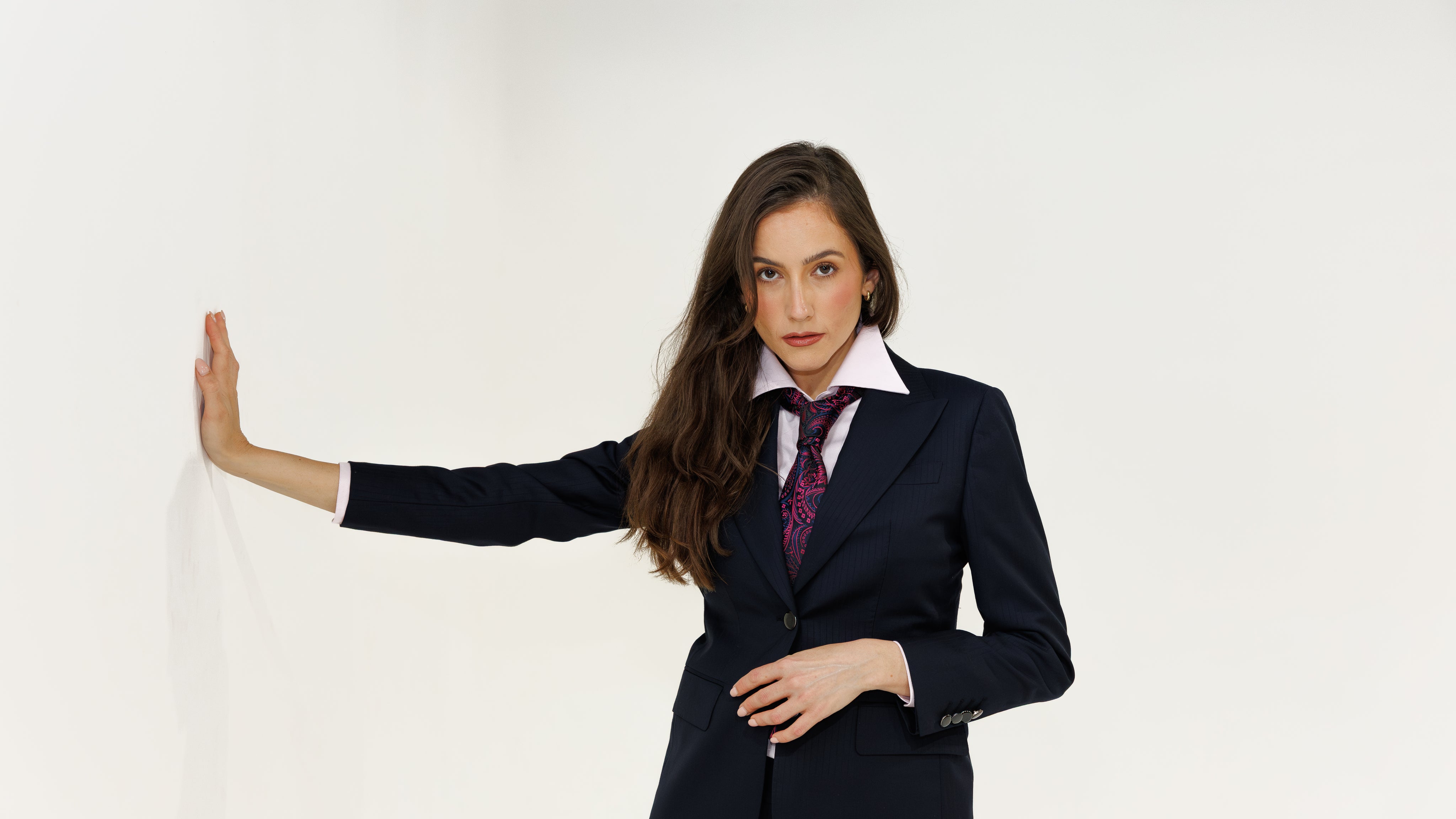 Woman wearing a navy suit with a white shirt and patterned tie on a plain background