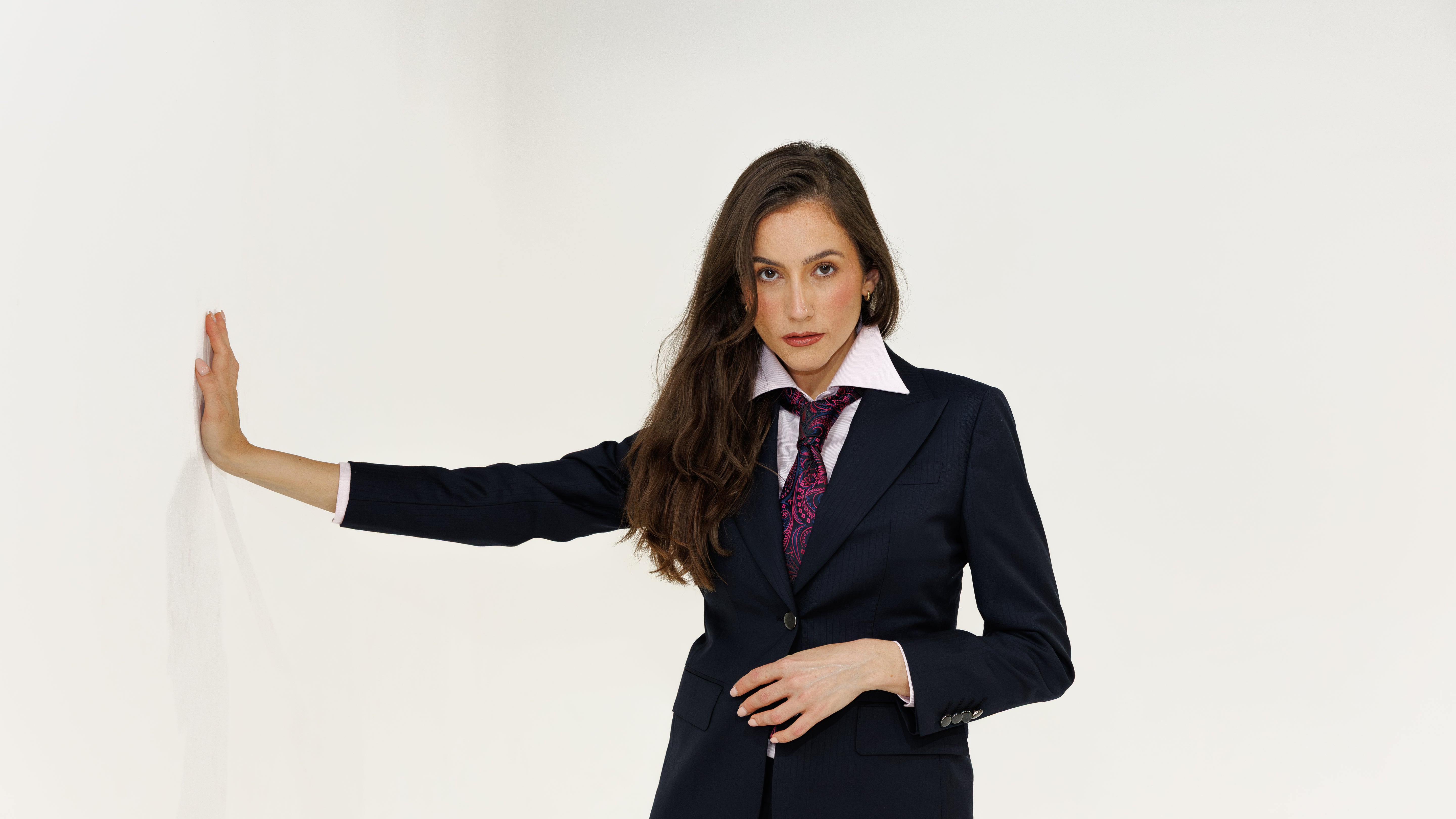 Woman wearing a navy suit with a white shirt and patterned tie on a plain background
