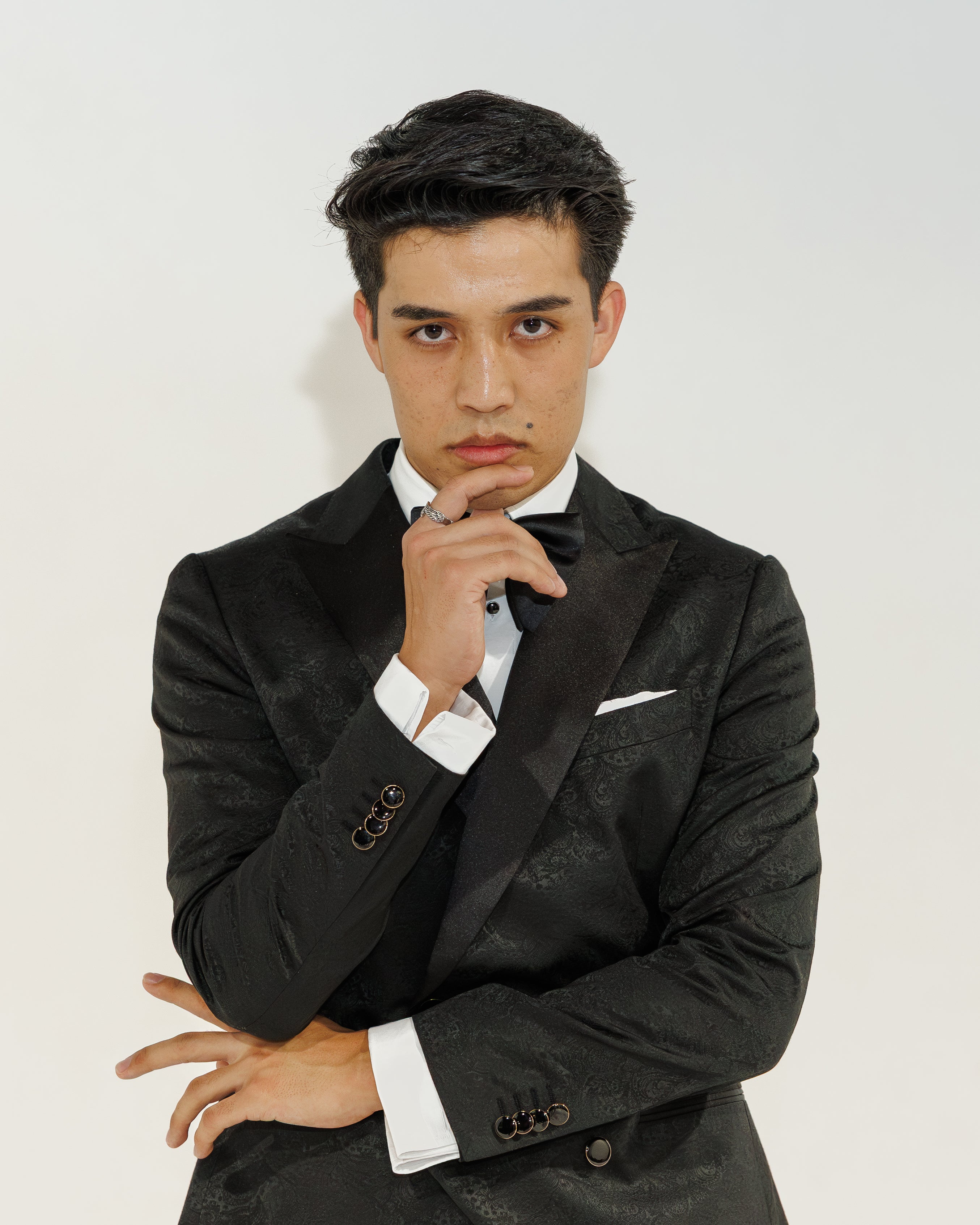 Man in a black tux with a white shirt and bow tie on a plain background