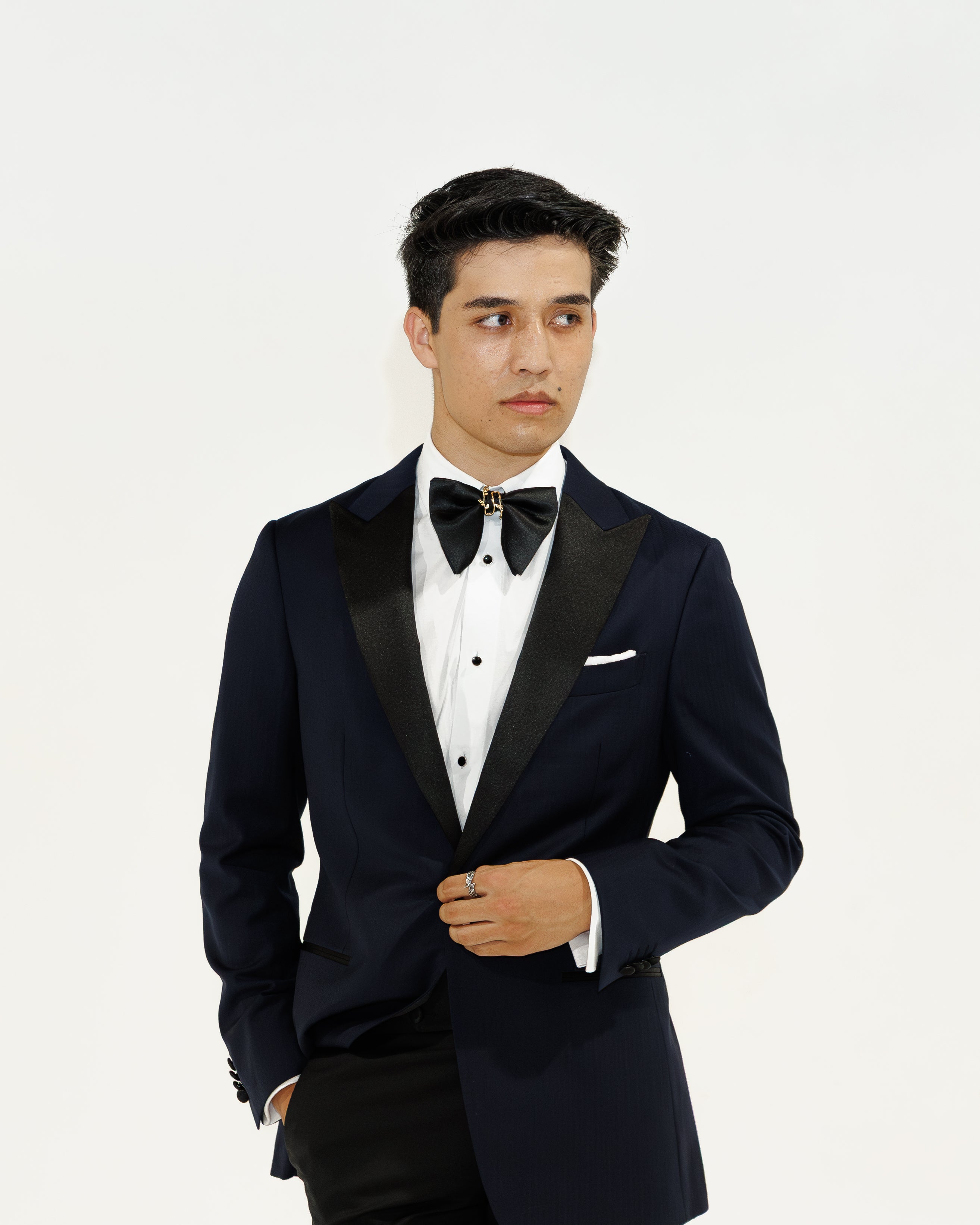 Man wearing a navy tuxedo with a white shirt and bow tie on a white background