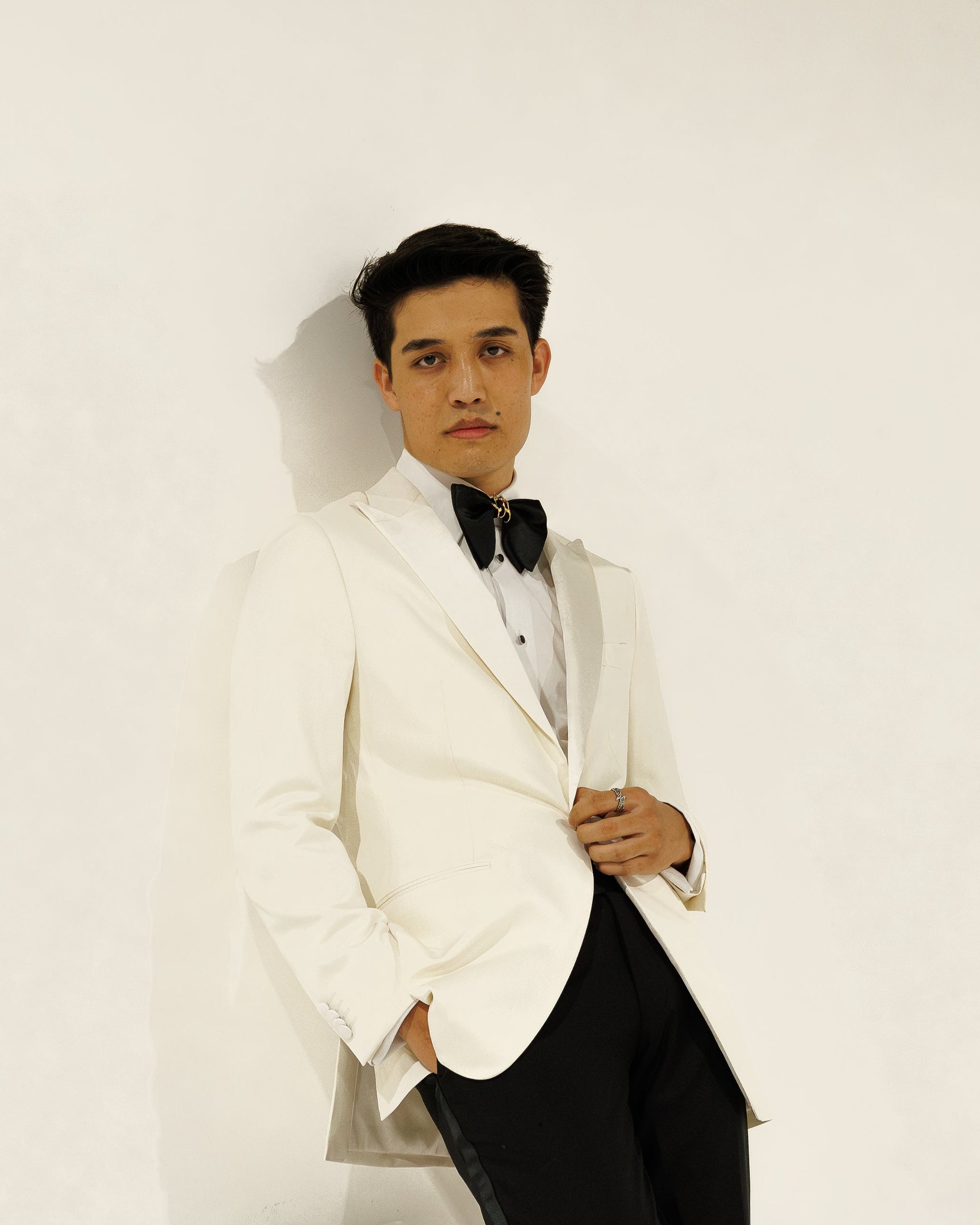 Man in a white tuxedo with black bow tie against a white background