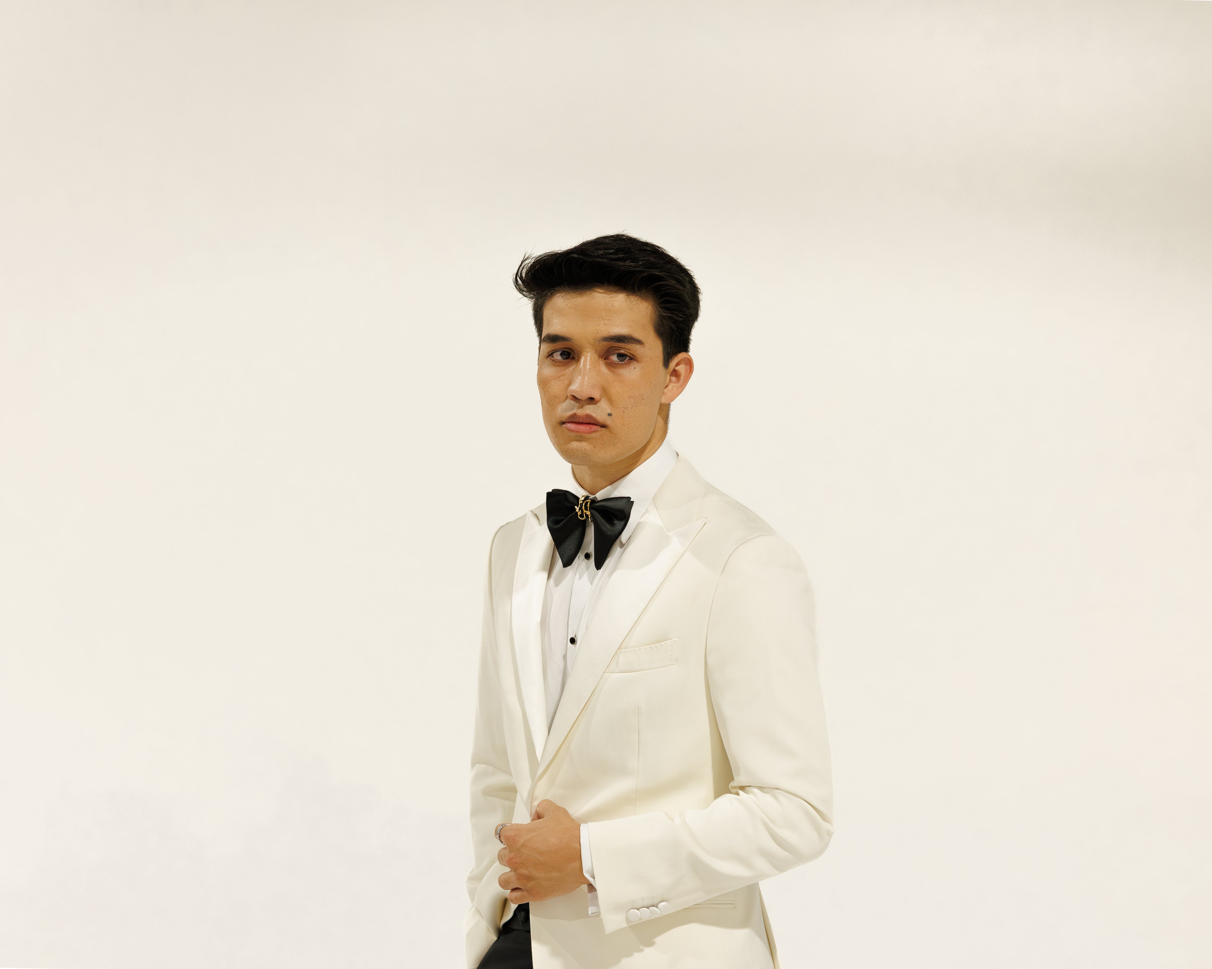 Man wearing a white tuxedo with a black bow tie against a plain background