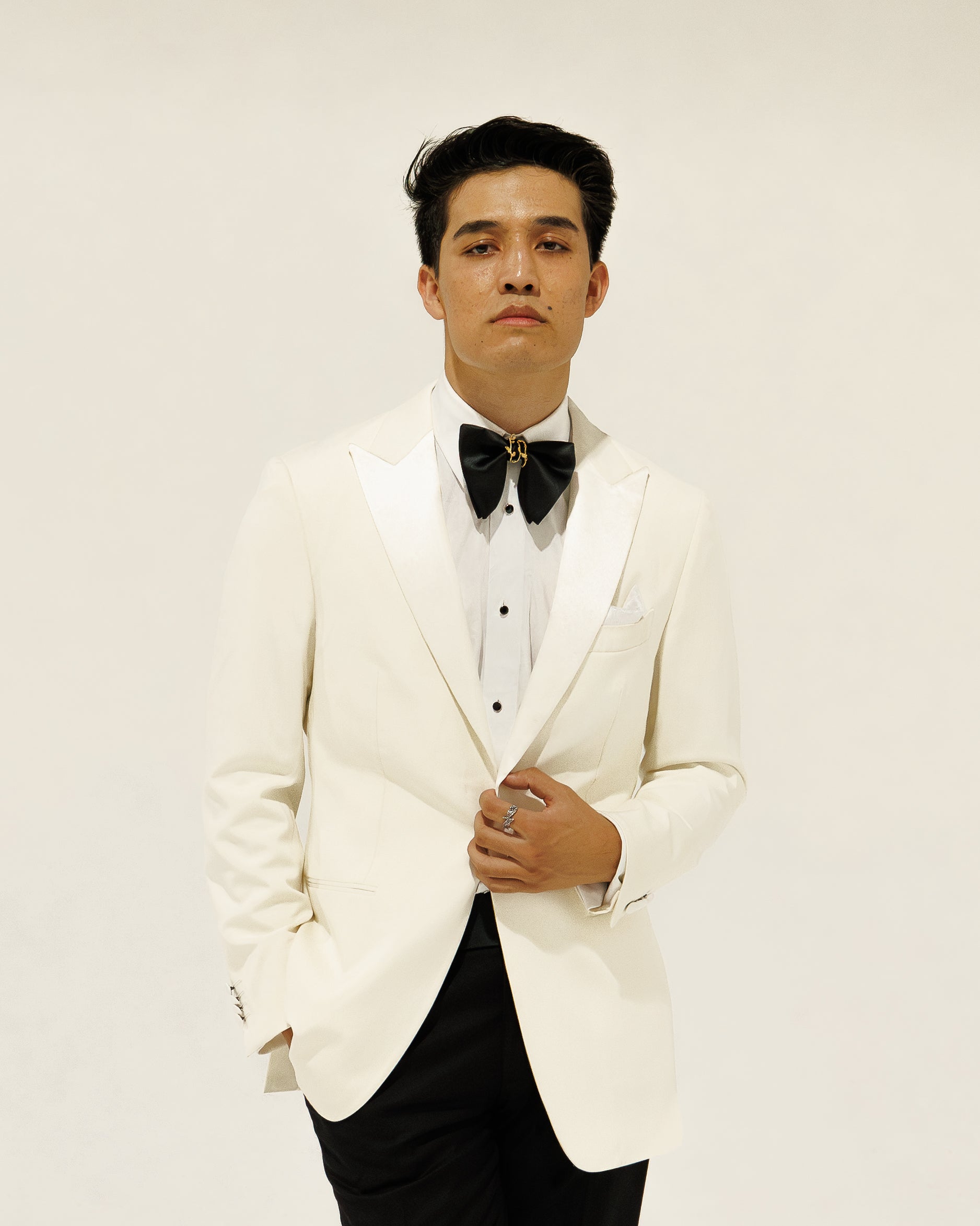Man wearing a white tuxedo with a black bow tie against a plain background