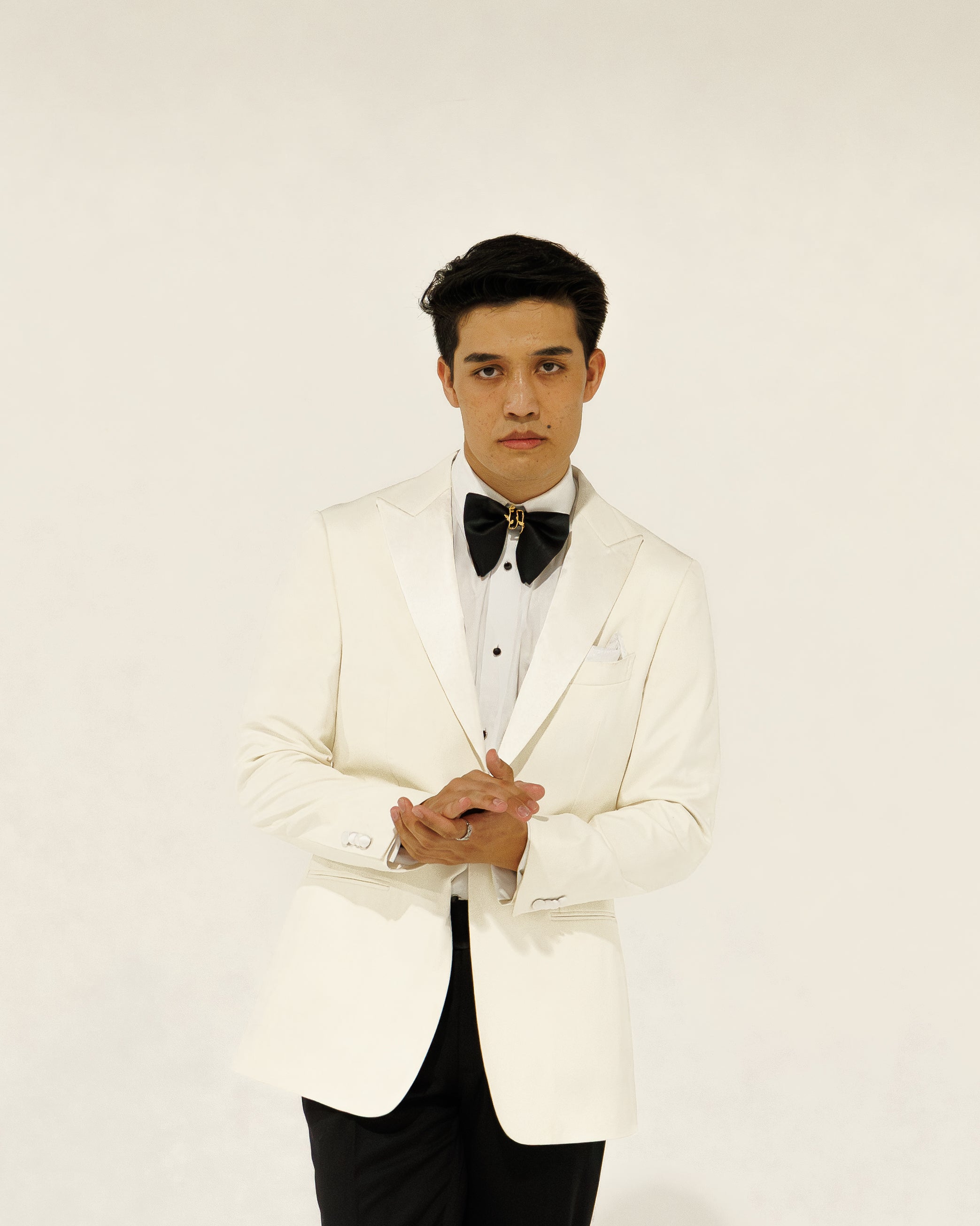 Man wearing a white tuxedo with a black bow tie against a white background