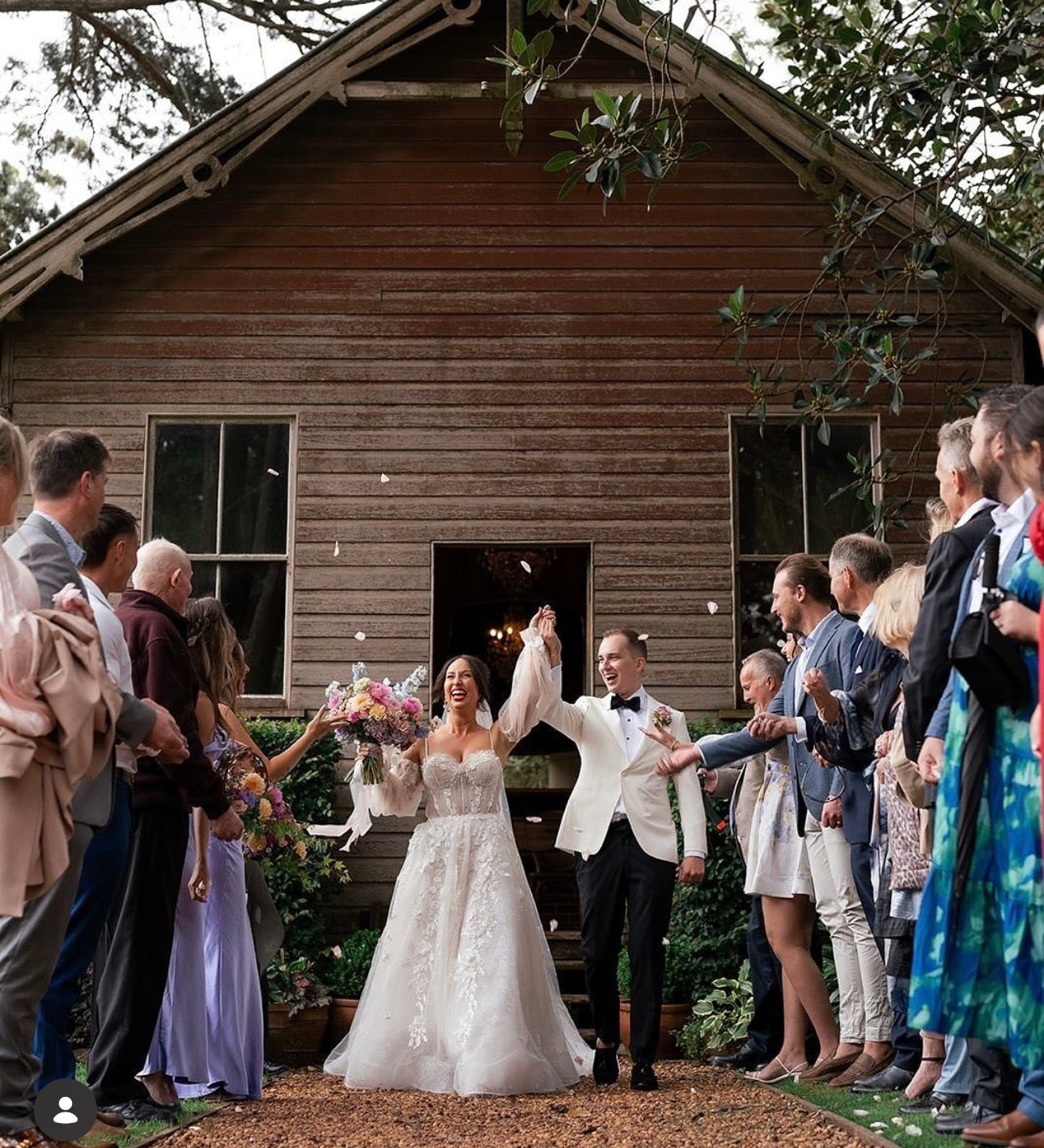 Wedding couple celebrating outside a wooden cabin with guests around.