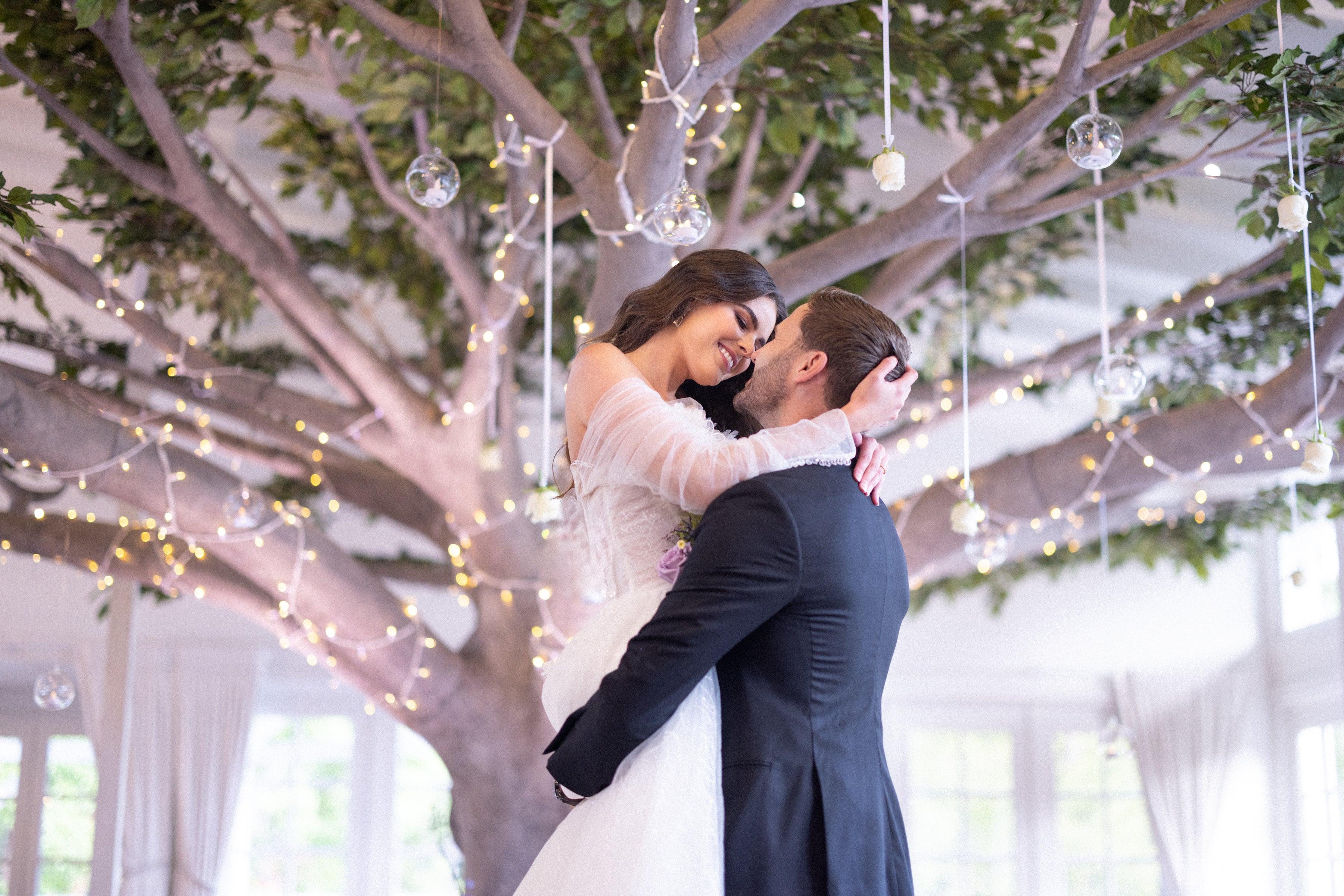 Couple embracing under a decorated tree with hanging lights and decorations.