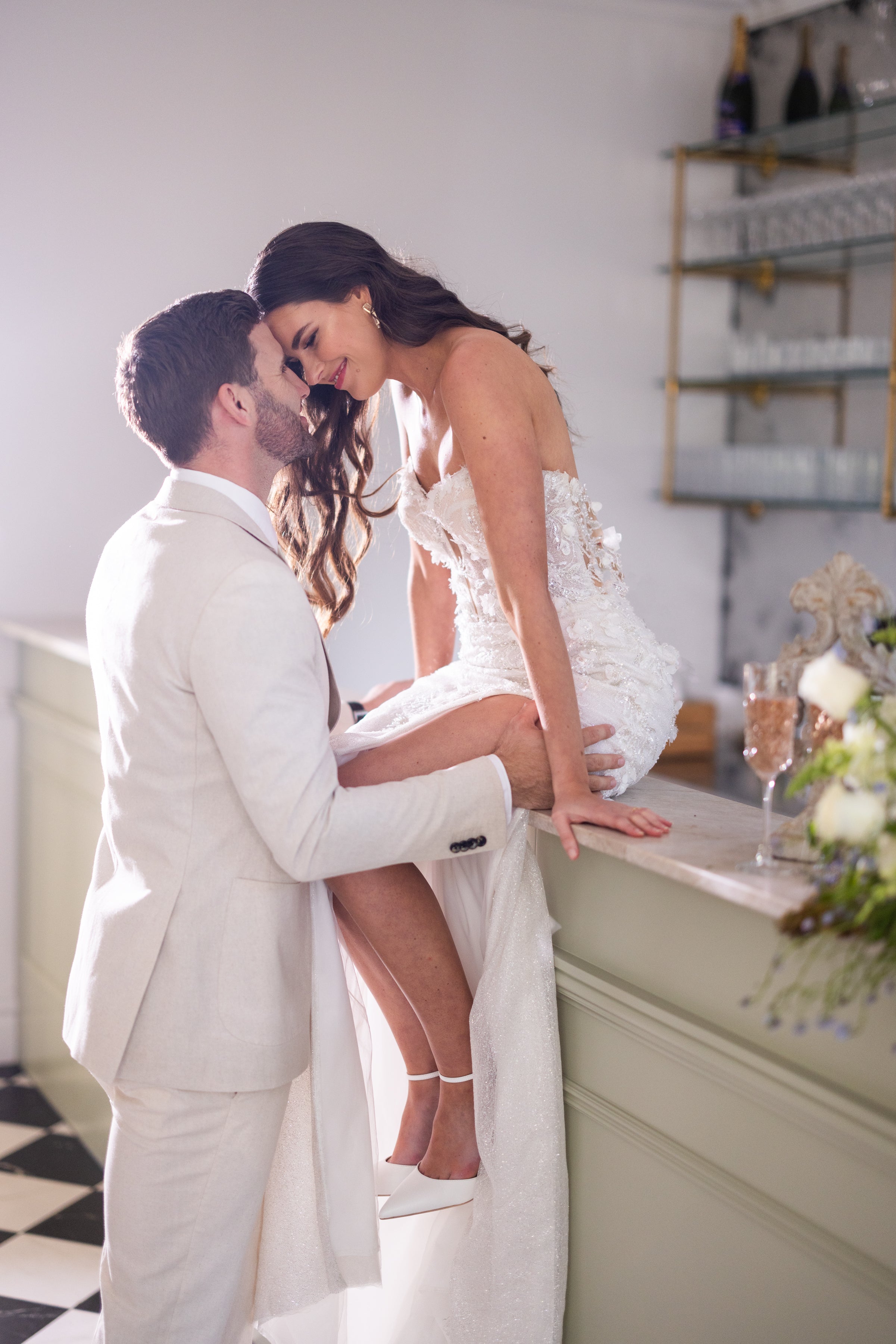 Man and woman in formal attire embracing in a kitchen setting.