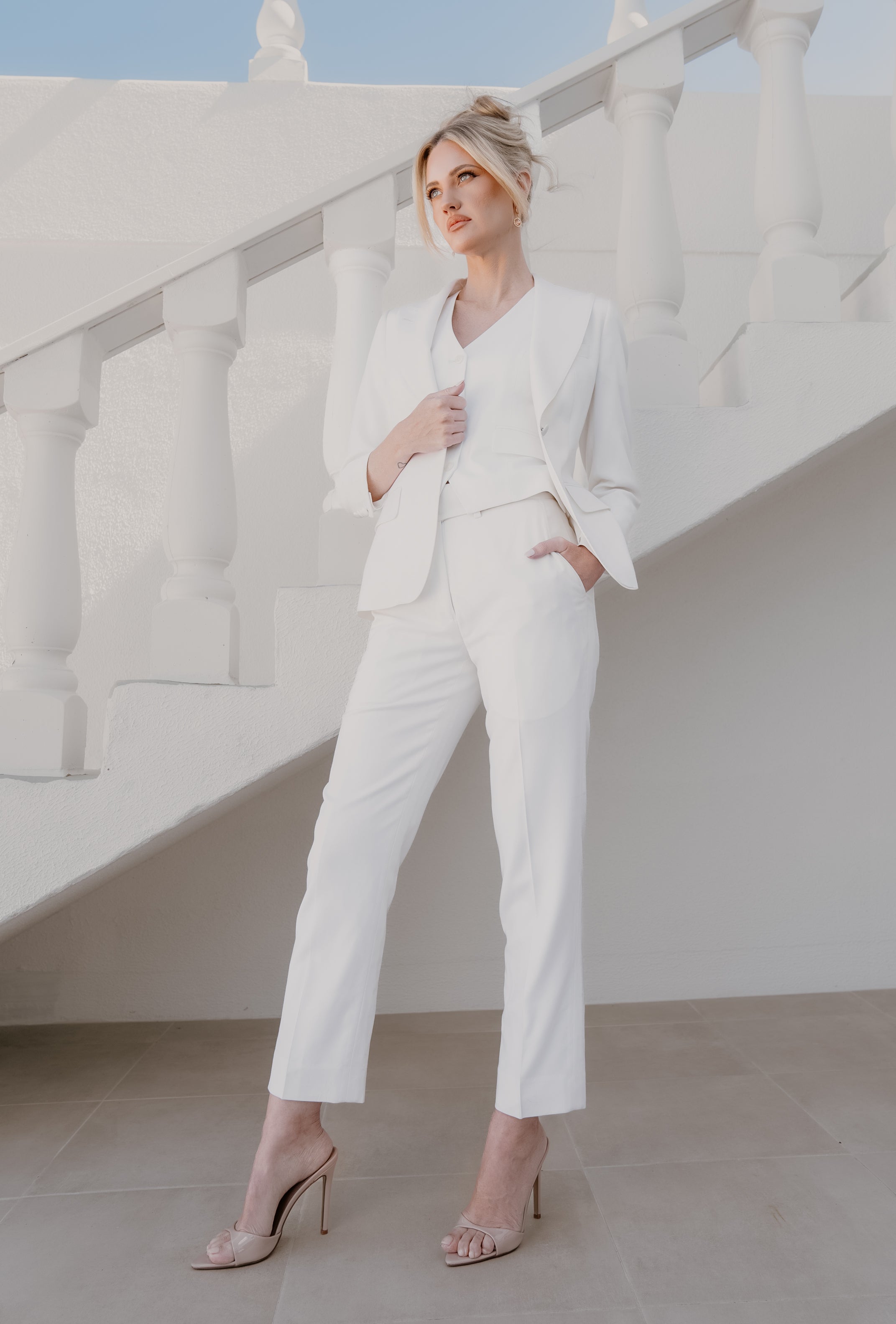 Woman in a white suit standing on a staircase with a clear sky background