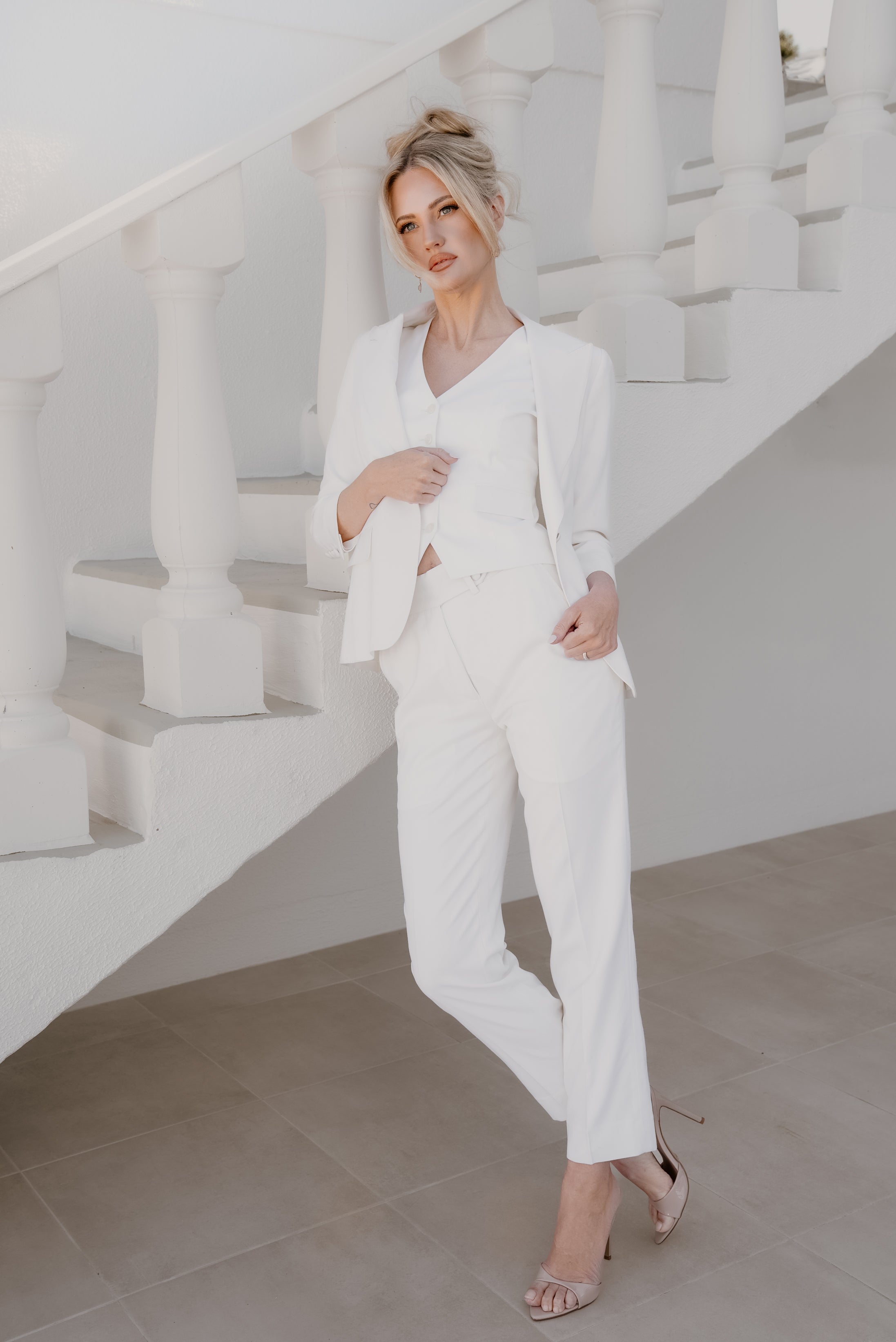 Woman in a white suit standing in a minimalistic setting with white stairs.