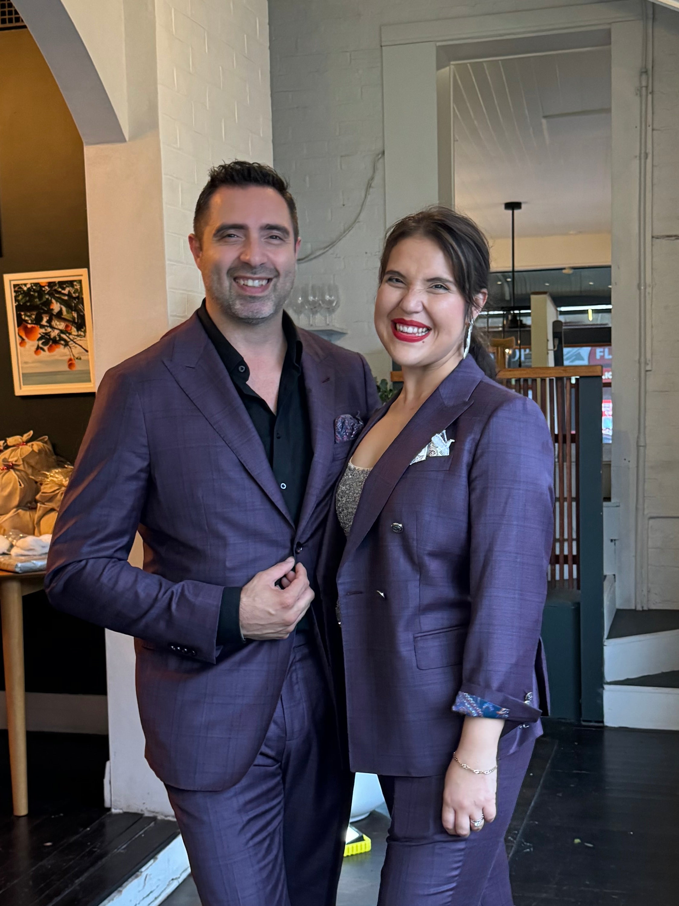 Two people in matching purple outfits standing in a modern indoor setting with a skylight.