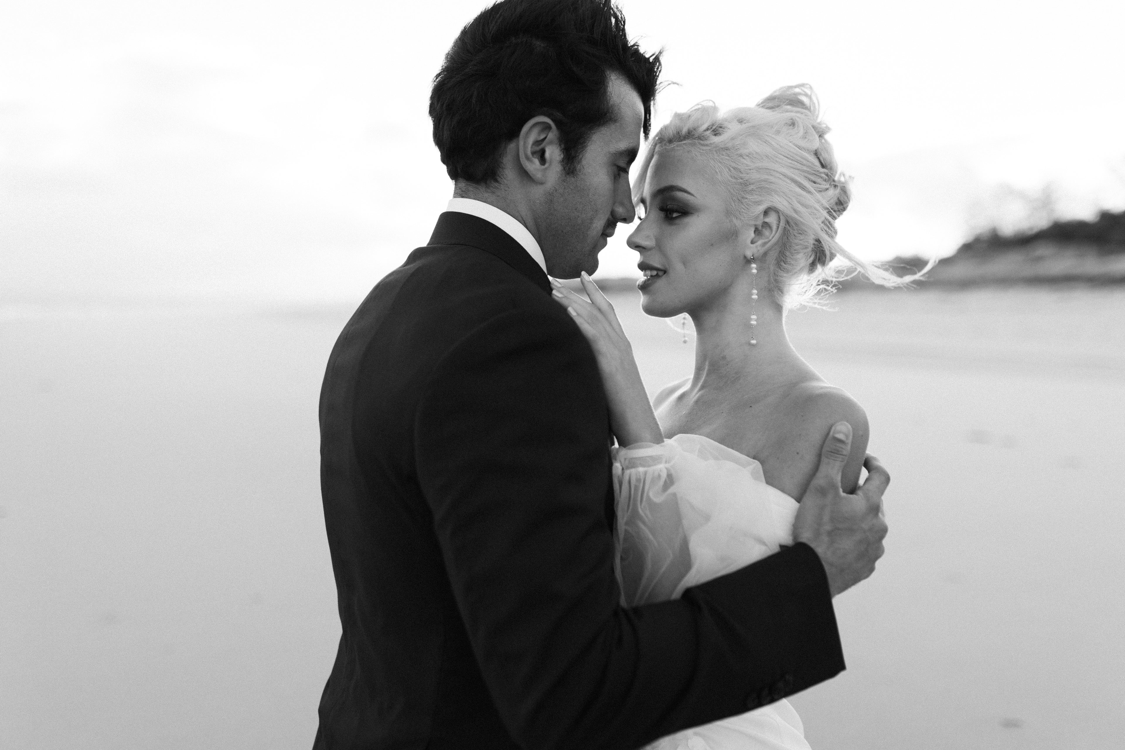 Black and white photo of a couple embracing by a body of water.