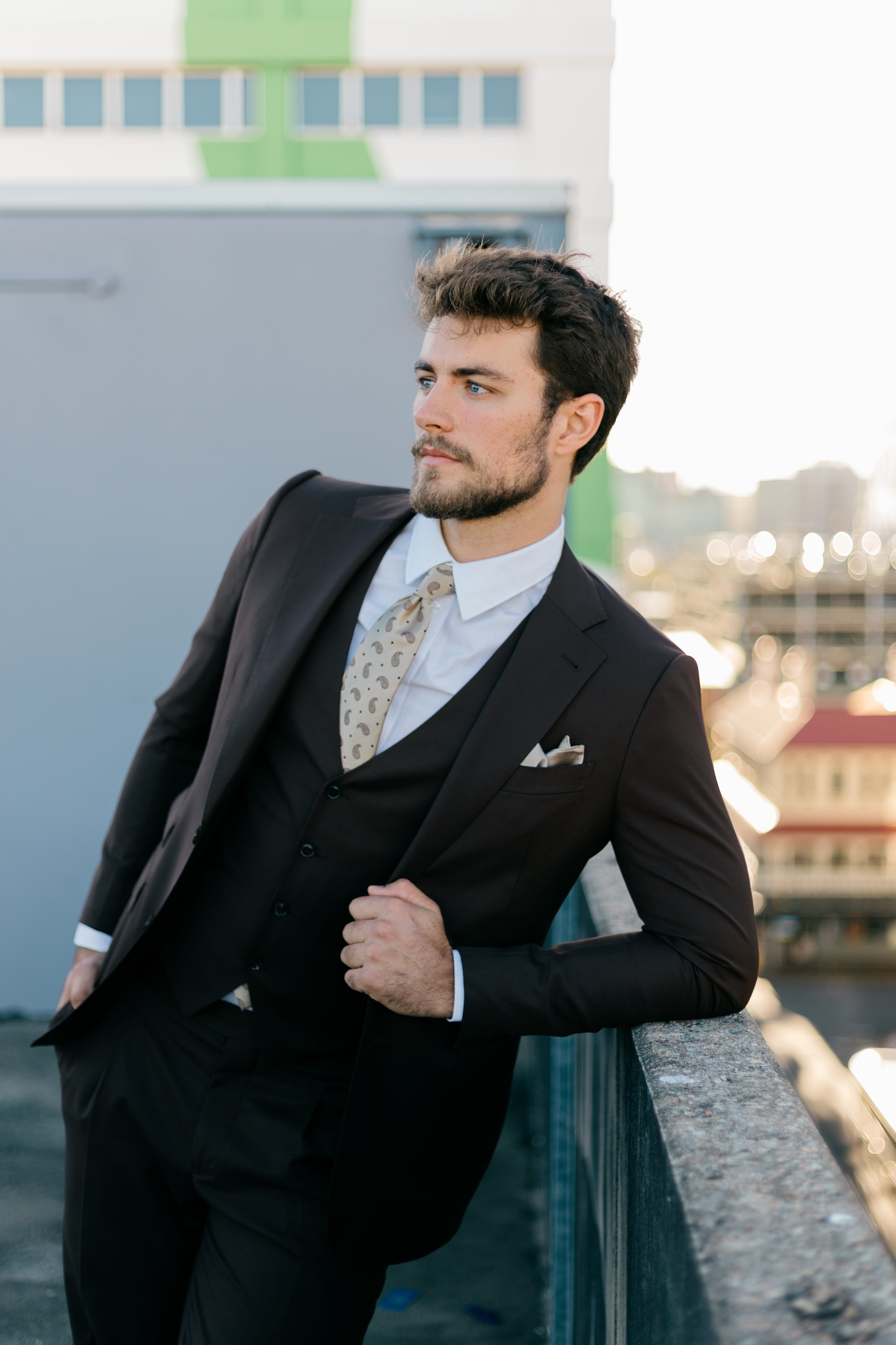 Man in a black suit with a patterned tie standing outdoors.