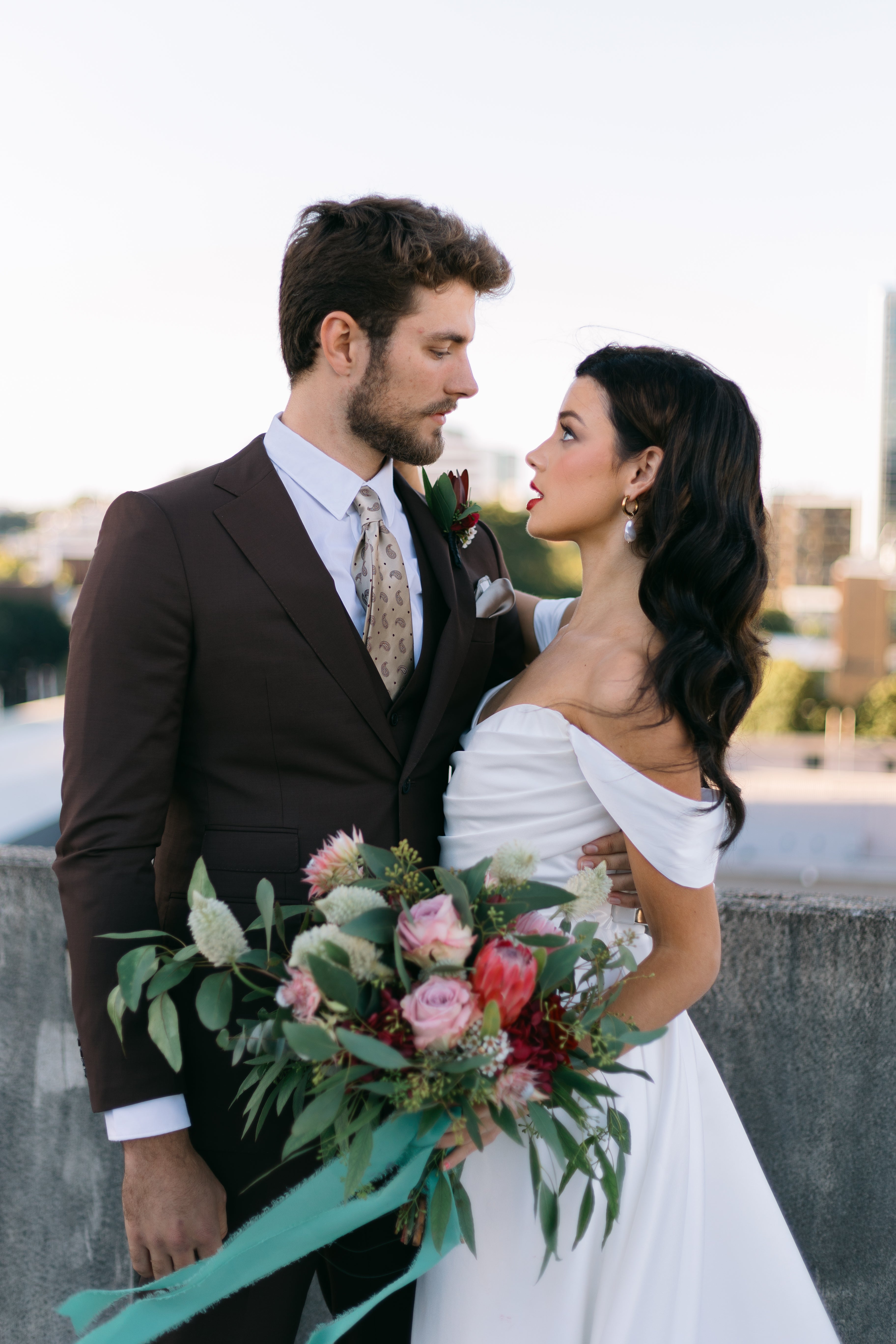 Man and woman in wedding attire holding a bouquet outdoors.
