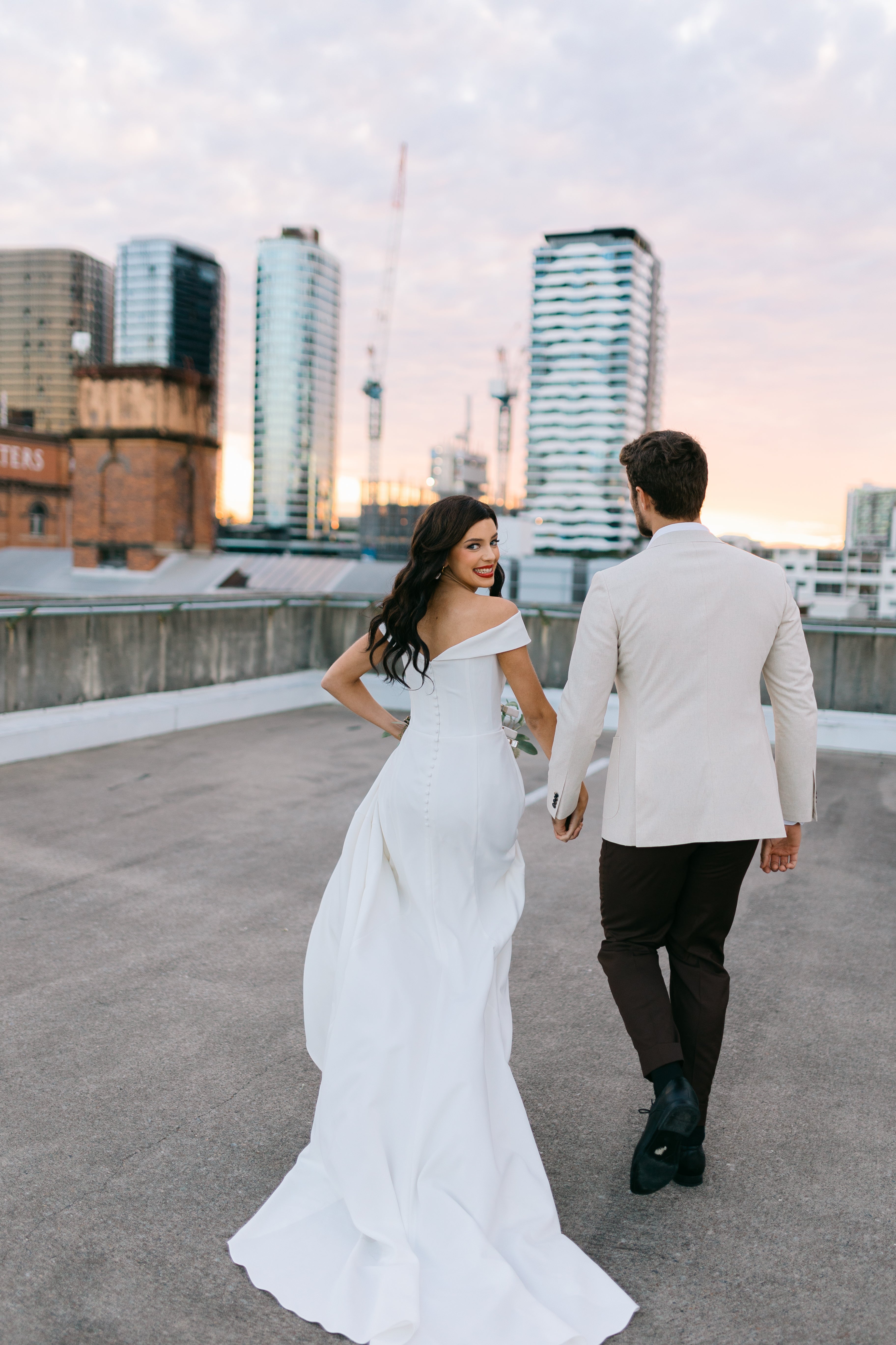 Couple in formal attire walking on a rooftop with city skyline in the background