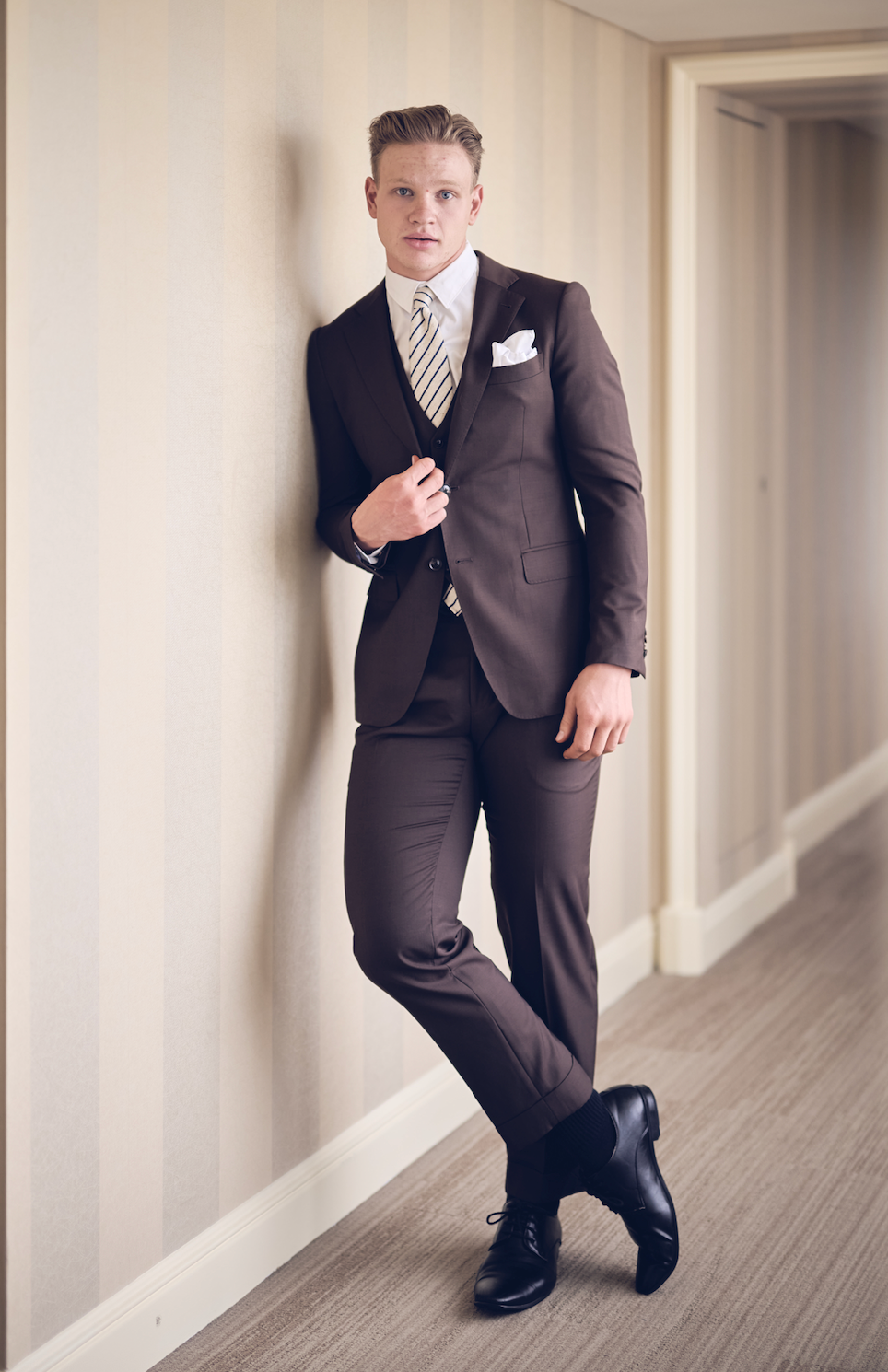 Man in a brown suit standing in a hallway