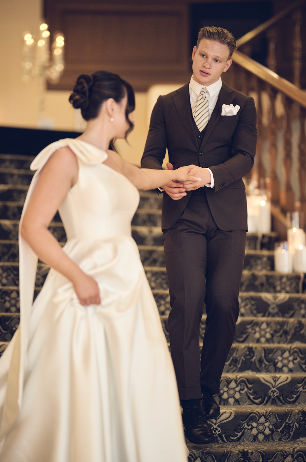 Man and woman in formal attire standing on a staircase with candles in the background