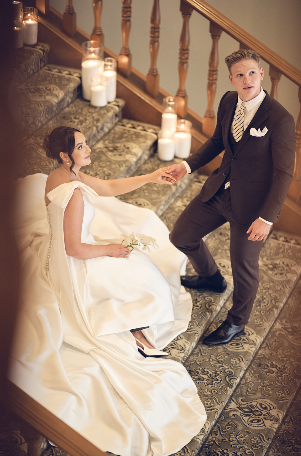 Man and woman in formal attire sitting on a staircase with candles around them