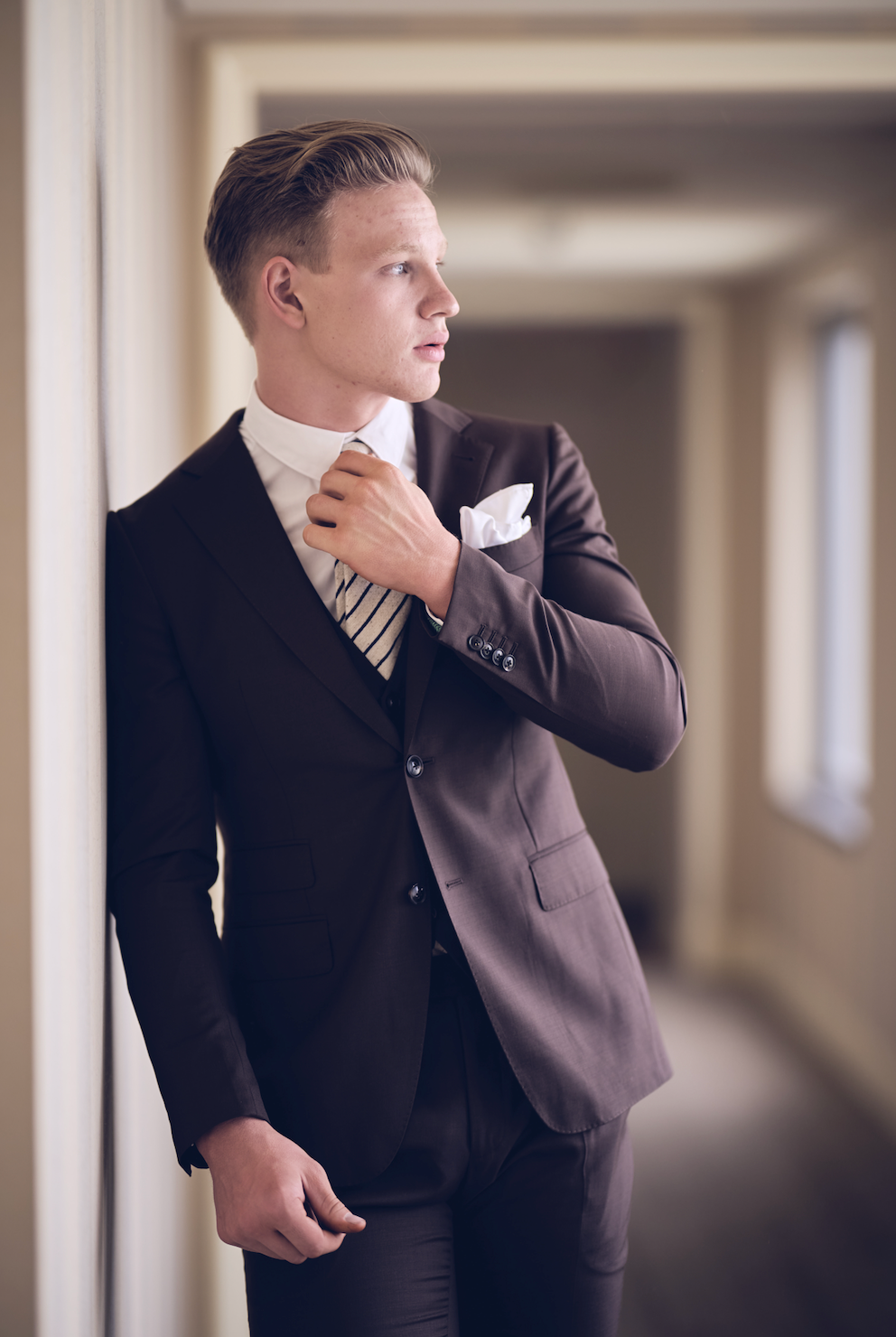Man in a formal suit adjusting his tie in an indoor setting