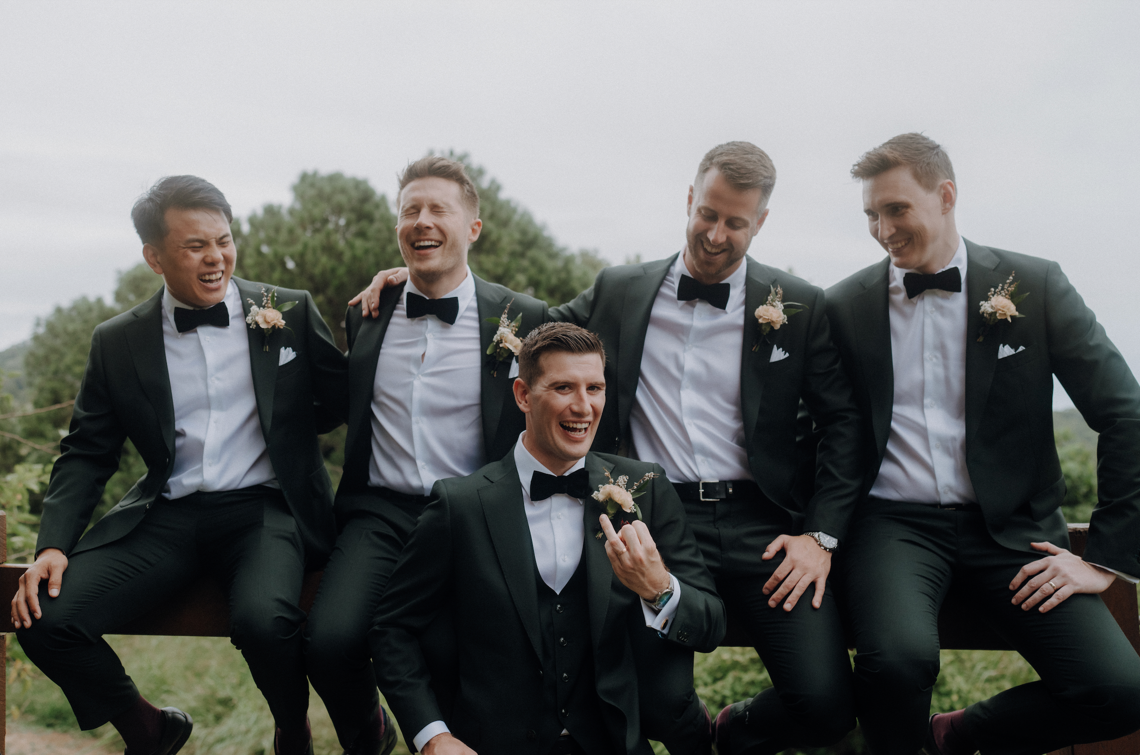 Four men in formal suits with bow ties sitting outdoors.
