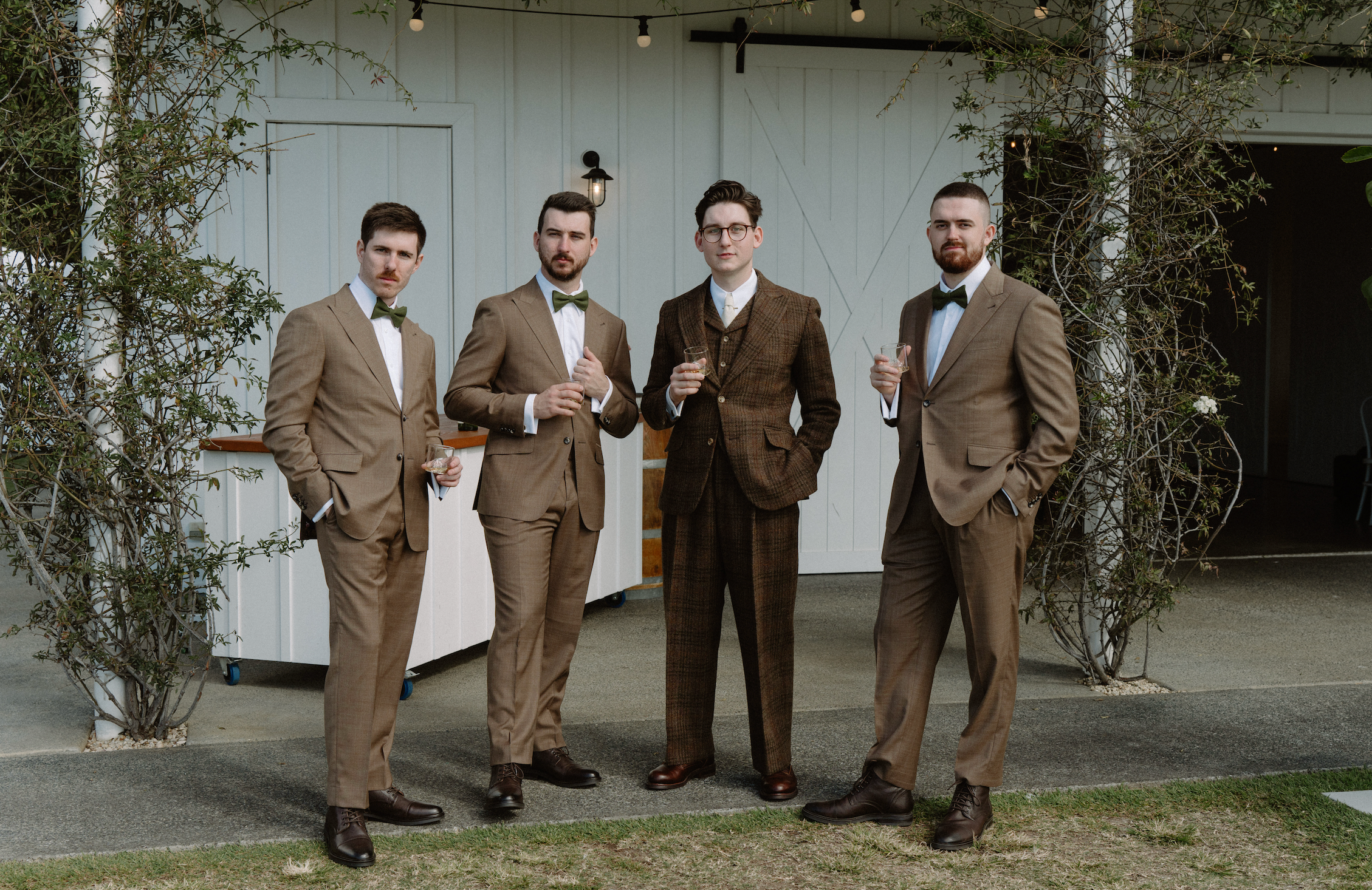 Four men in brown suits standing outdoors with a white building in the background.